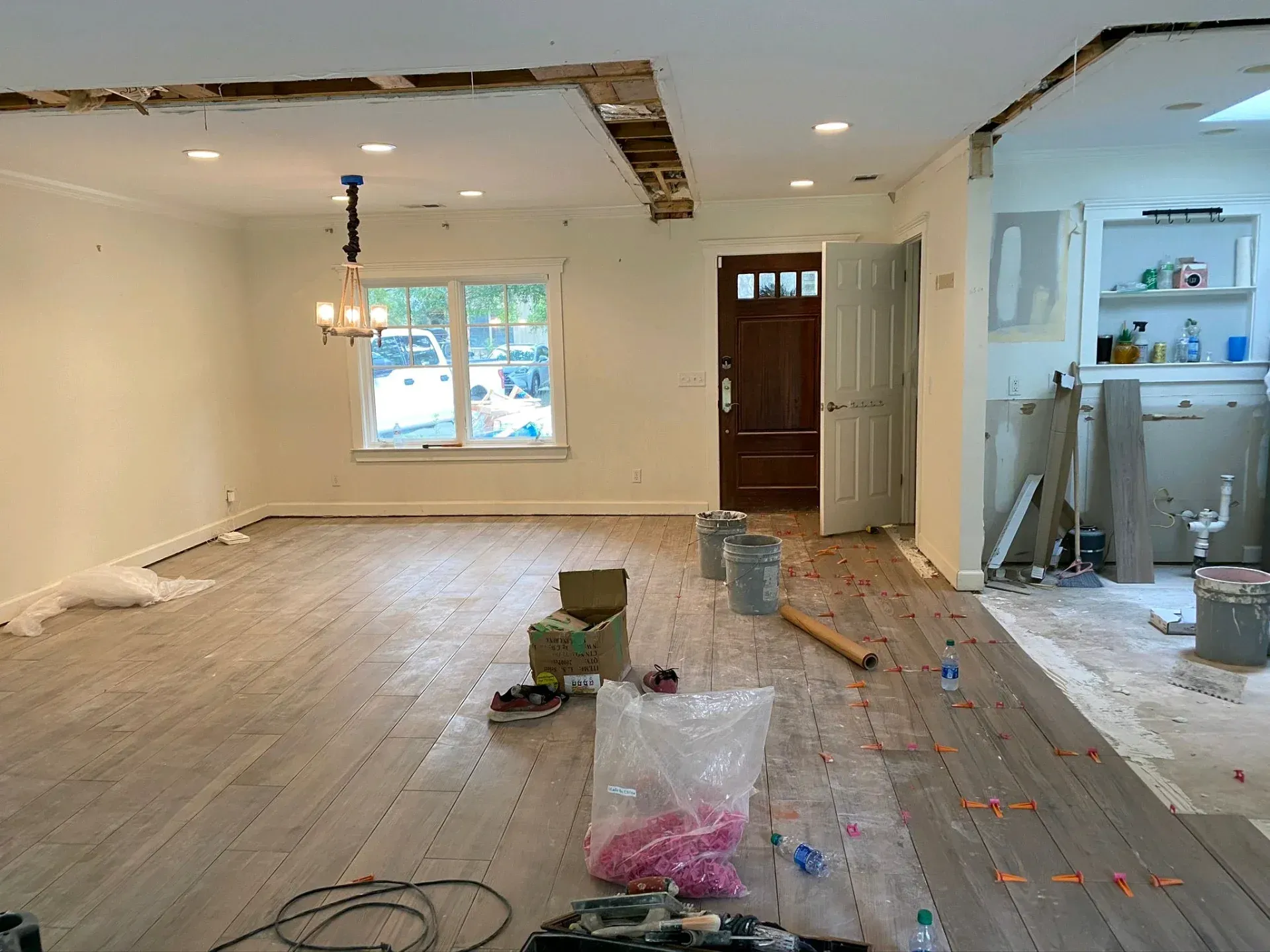 Renovated living room with exposed ceiling beams, unfinished floor, tools, and a doorway to a kitchen area