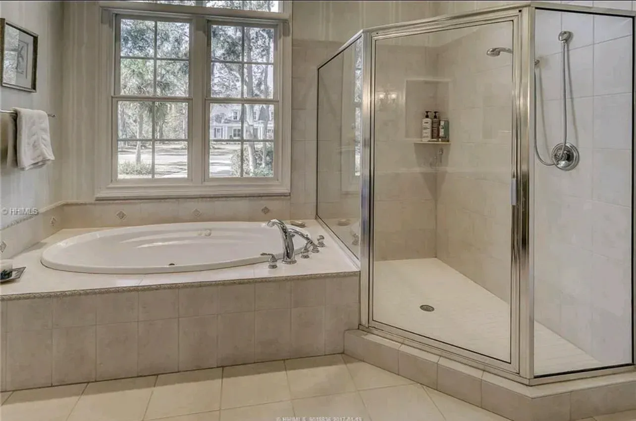 Bright bathroom with a bathtub, glass shower, and large window with white tile walls.
