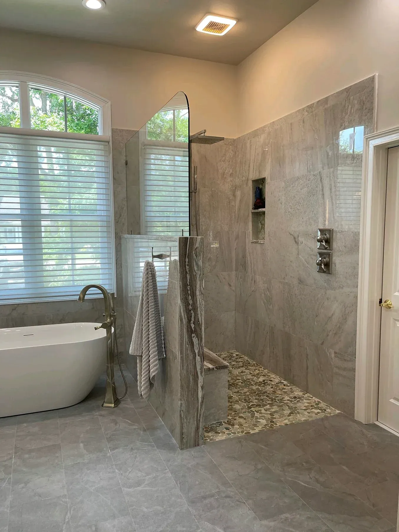 Modern bathroom with freestanding tub, glass shower, gray tile, and large window blinds