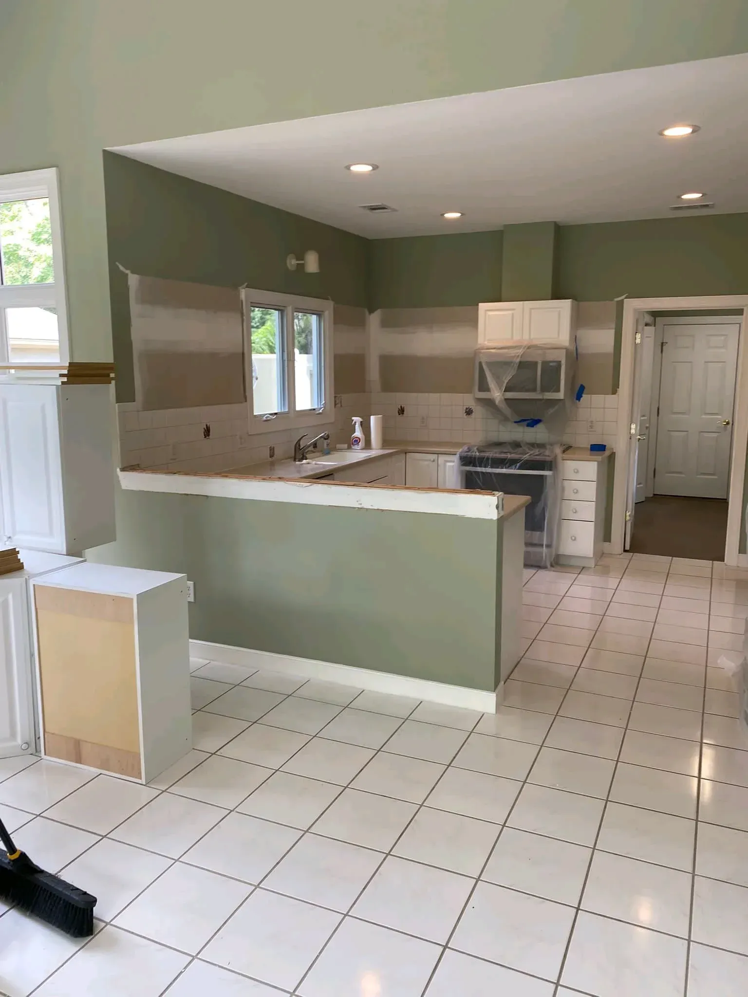 Empty kitchen with green walls, white tile floor, white cabinets, and a pass-through counter.