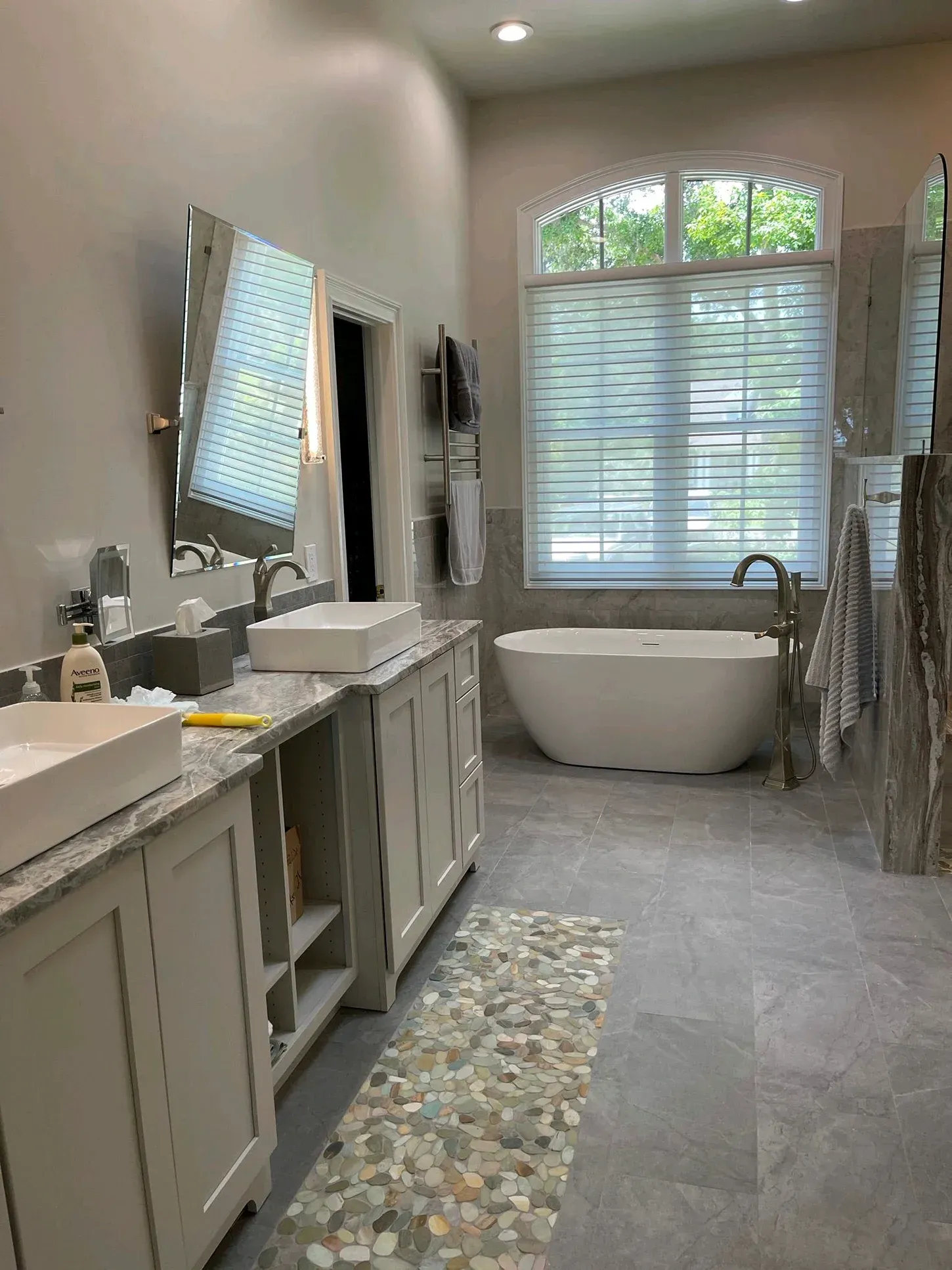 Modern bathroom with double vanity, freestanding tub, and window with blinds