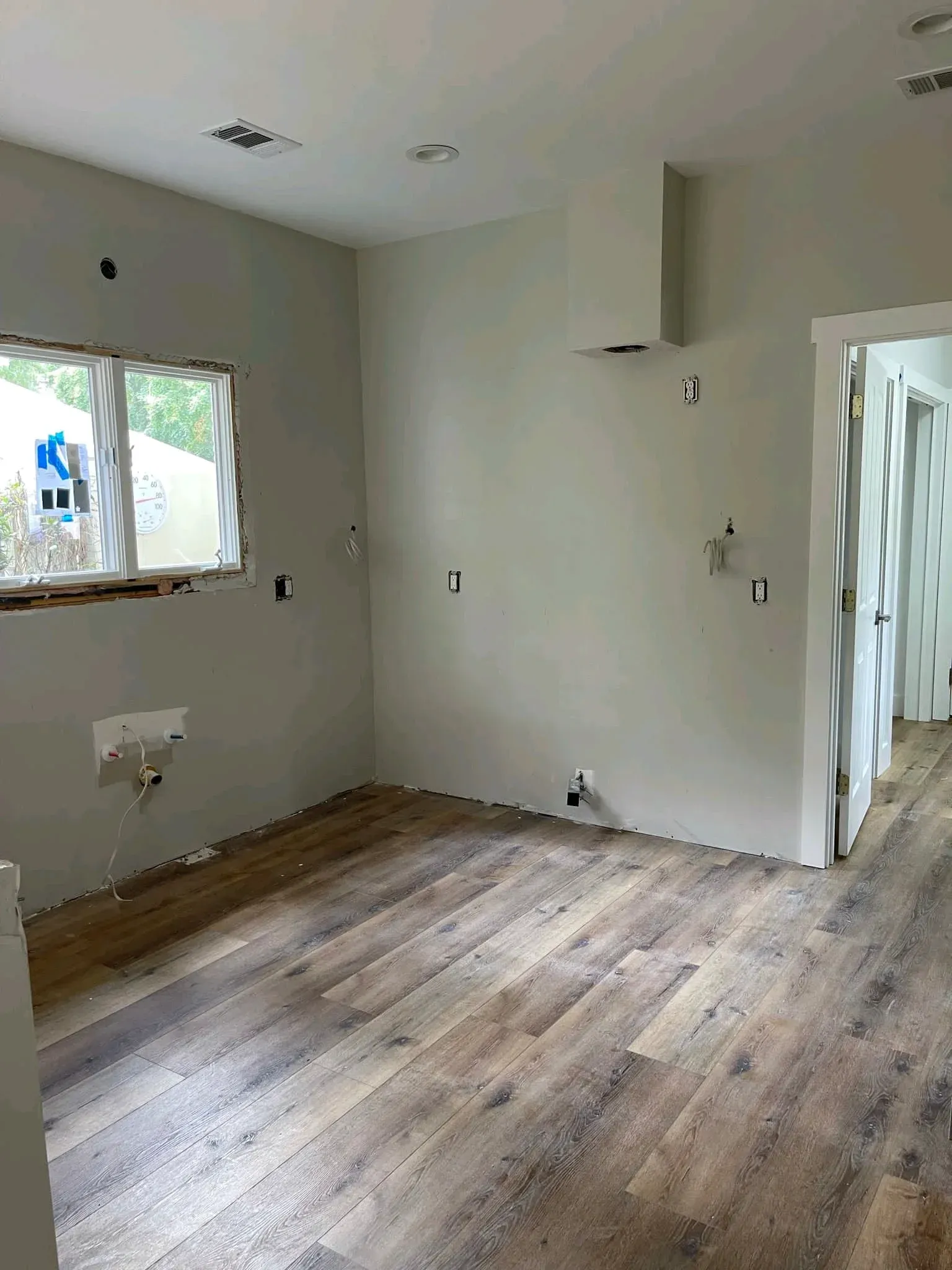Empty room with white walls, wood-look flooring, and a window letting in daylight.
