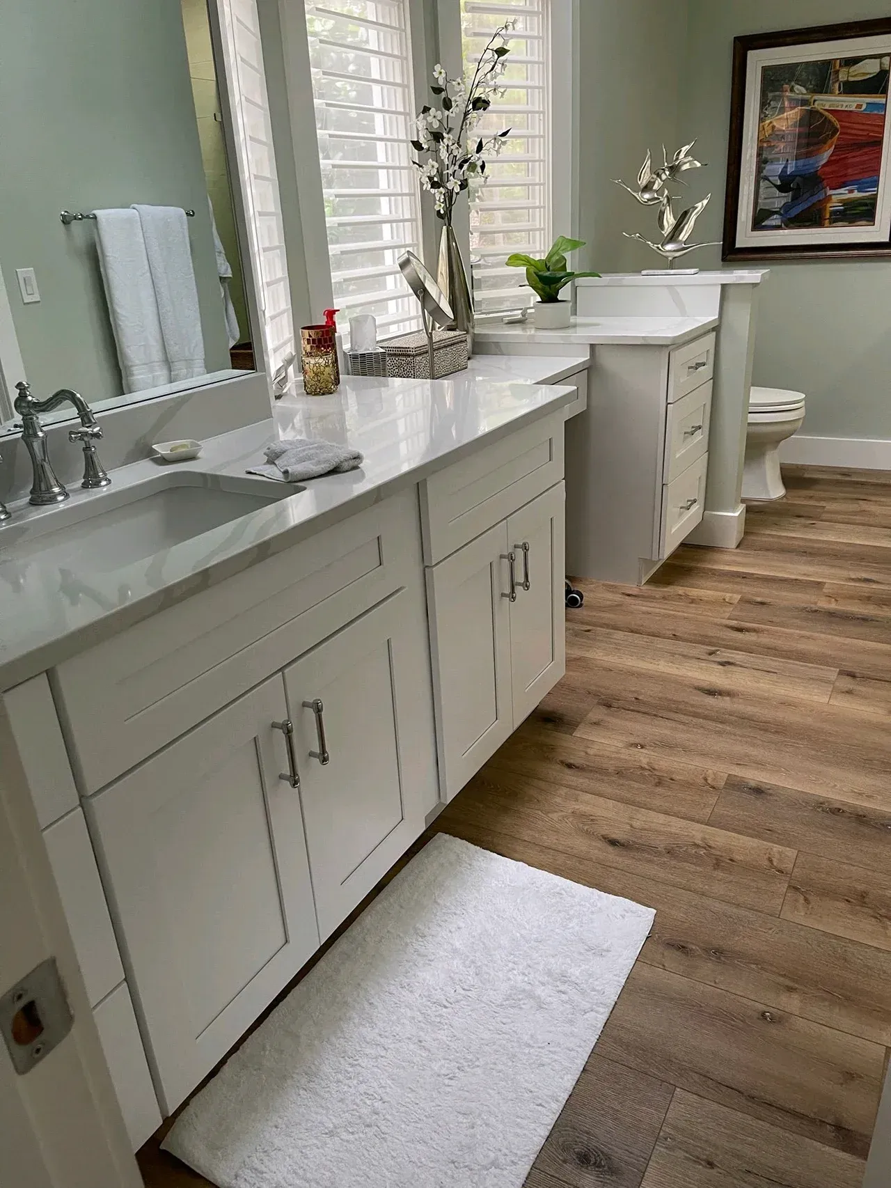 Bright bathroom with white vanity, double sinks, large mirror, window, and wood-look floor.