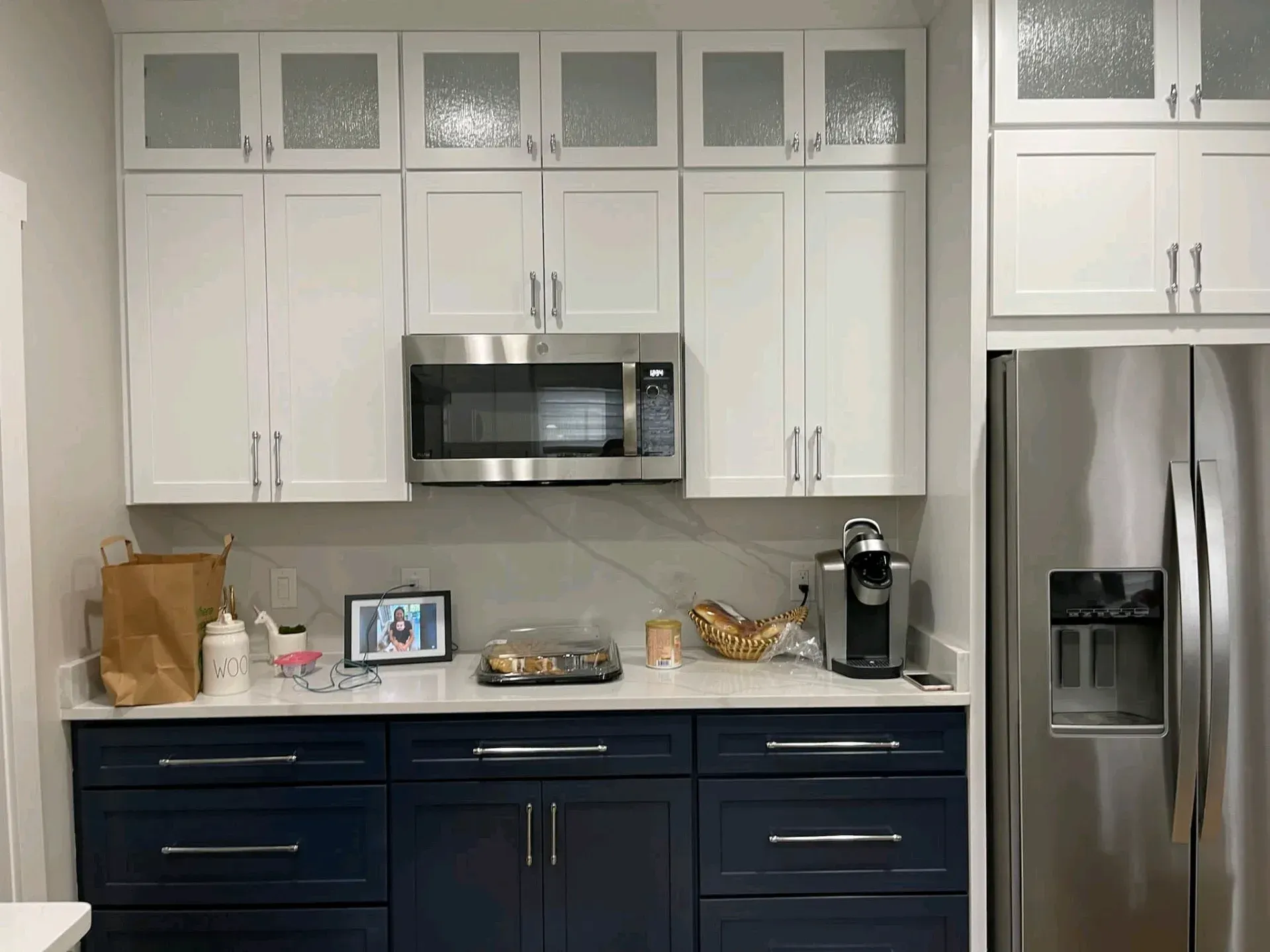 Modern kitchen with white cabinets, dark blue lower cabinets, stainless steel appliances, and countertop decor