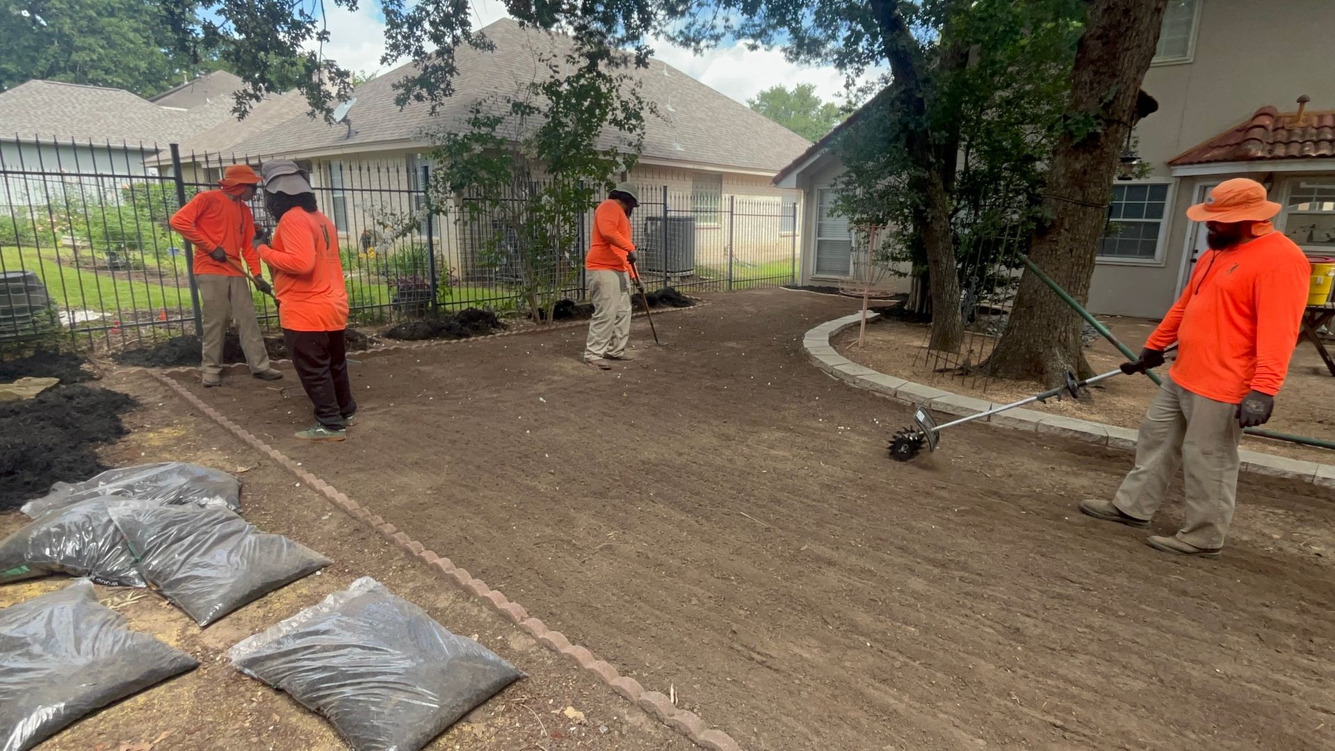 Landscapers in orange shirts and hats laying mulch in a yard with bags of mulch.