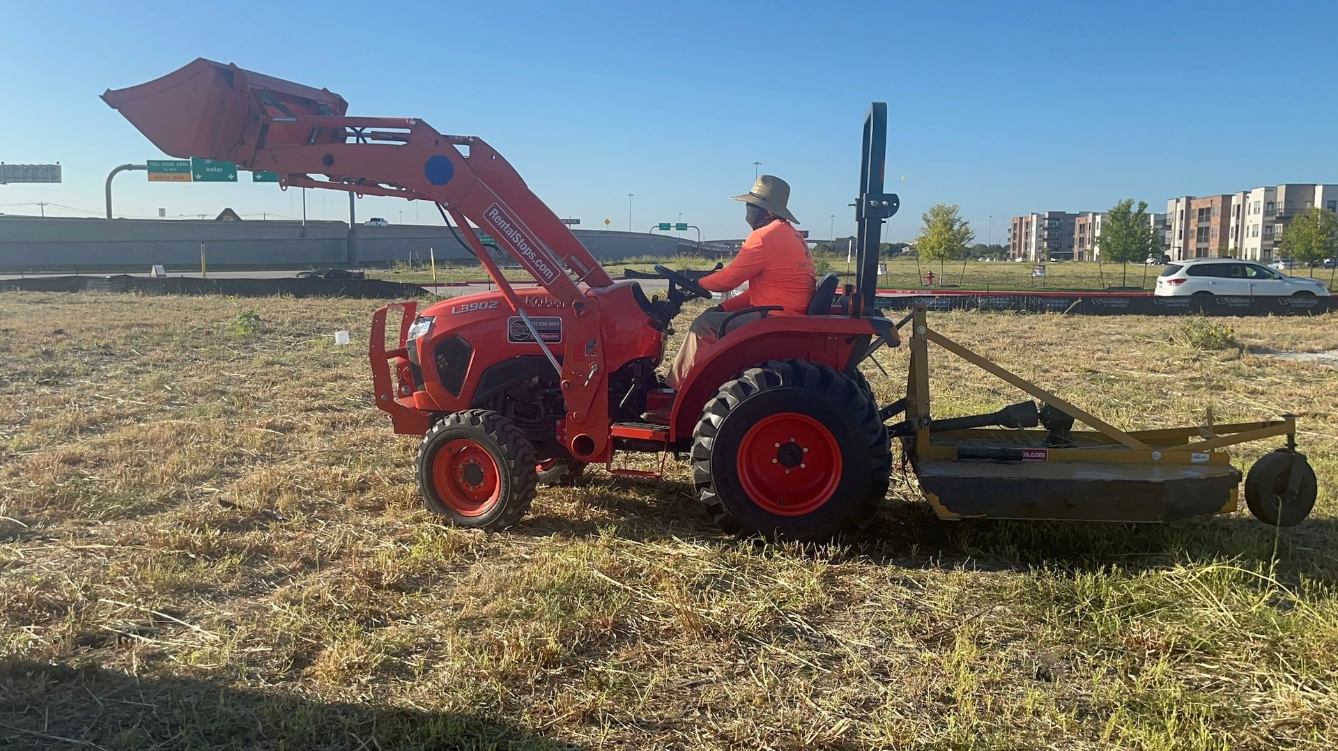 Orange tractor mowing roadside weeds with driver.
