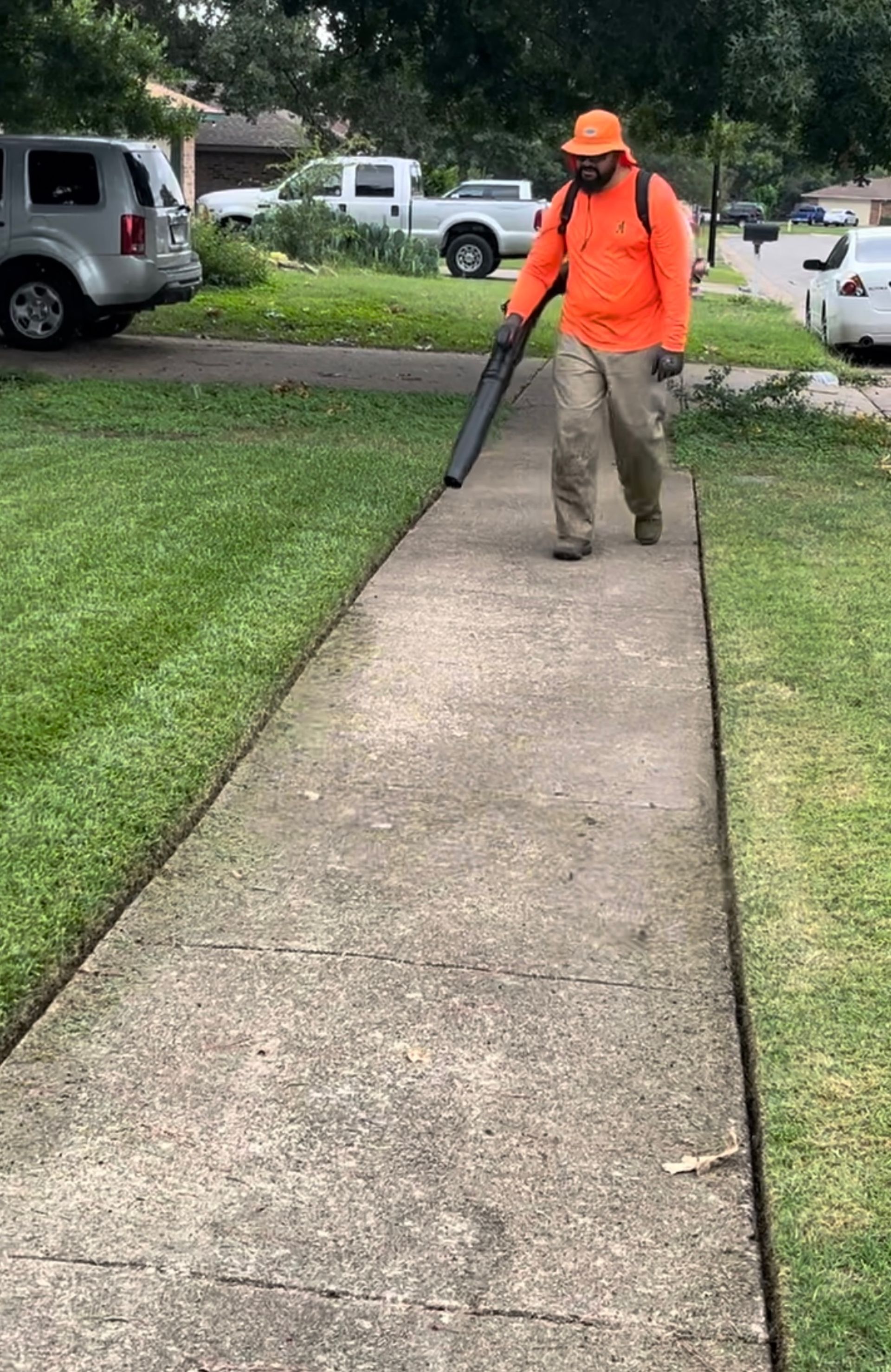 Person in orange blowing leaves off a sidewalk.