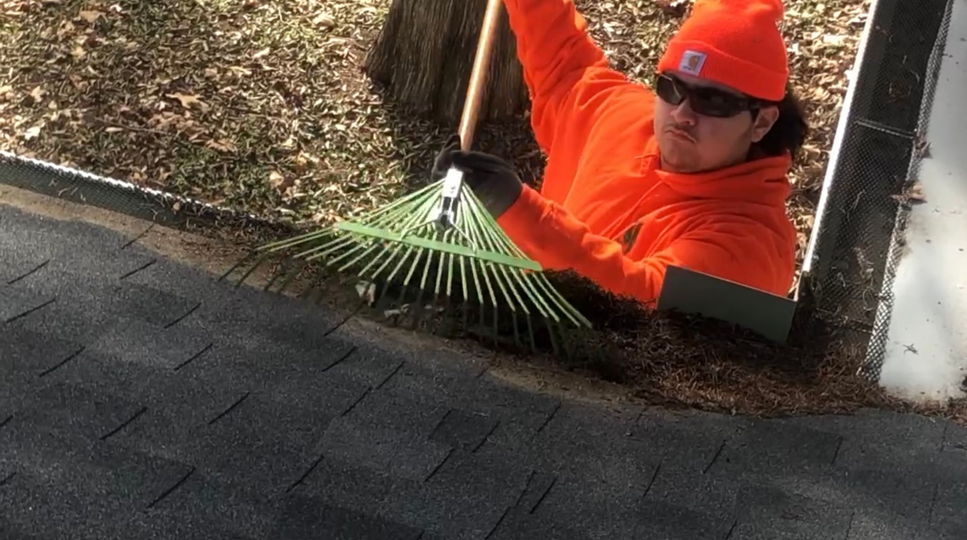 Person in orange raking leaves from a gutter on a roof.
