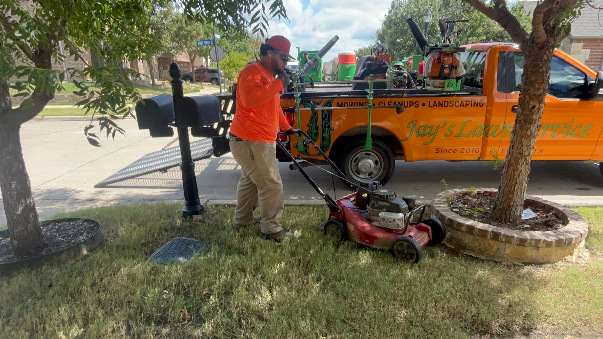 Man in orange shirt mowing grass with a red lawnmower near an orange truck.