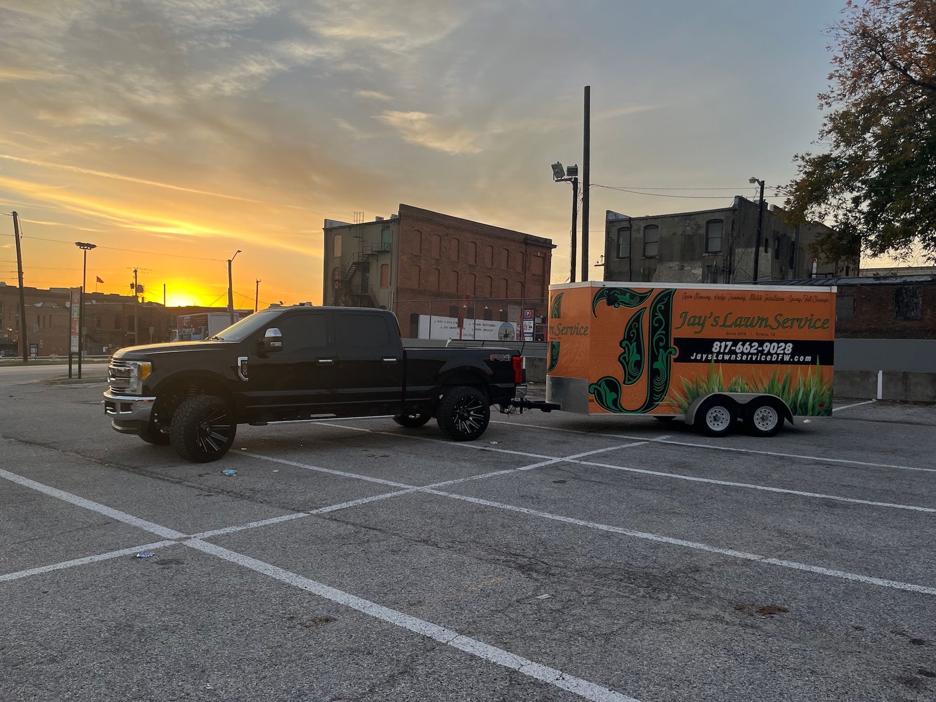 Black truck with a trailer, in a parking lot at sunset.