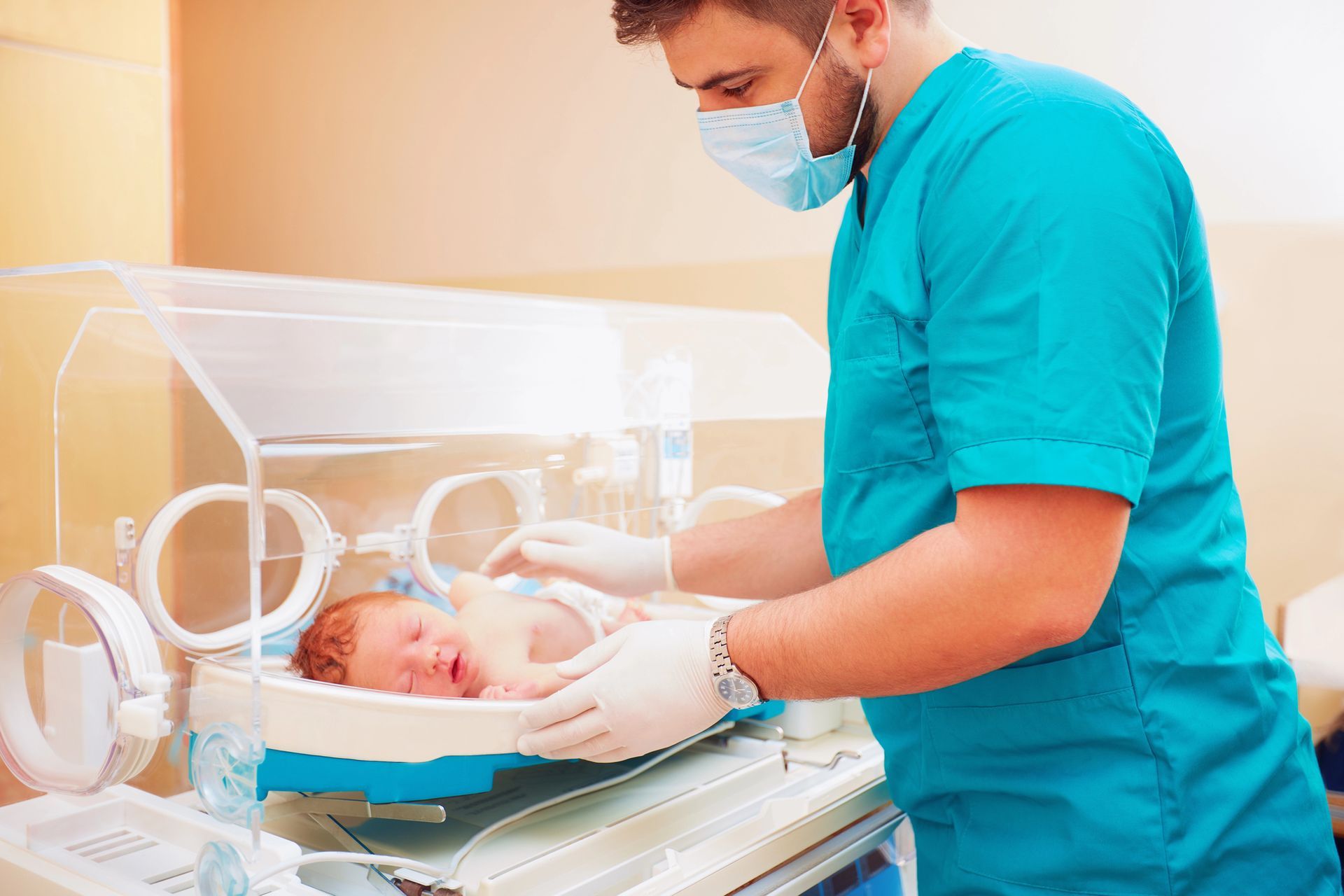 Infermiera con mascherina che si prende cura di un neonato in un’incubatrice trasparente in ospedale