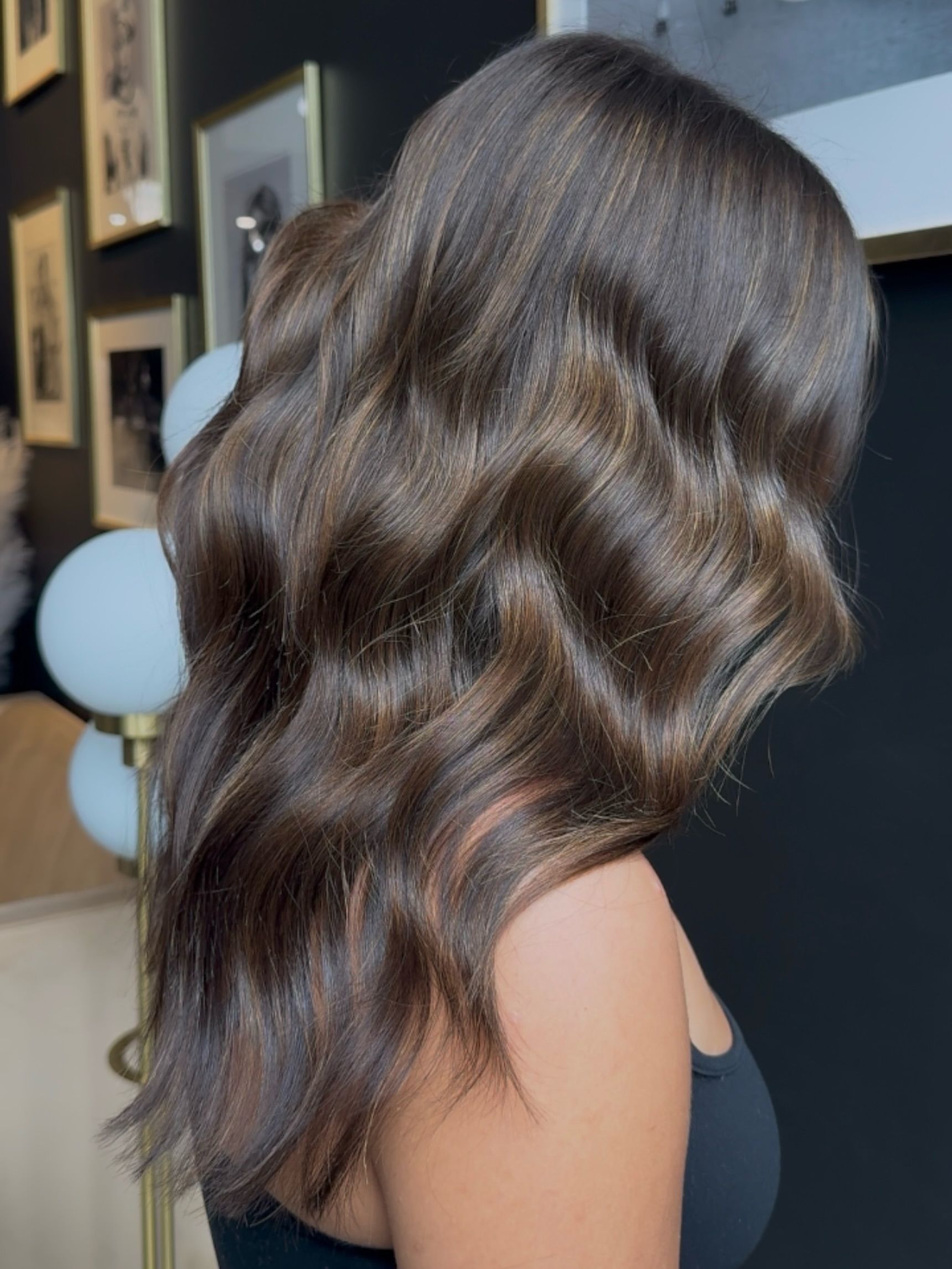 Side view of long, wavy dark brown hair with soft highlights in an indoor setting