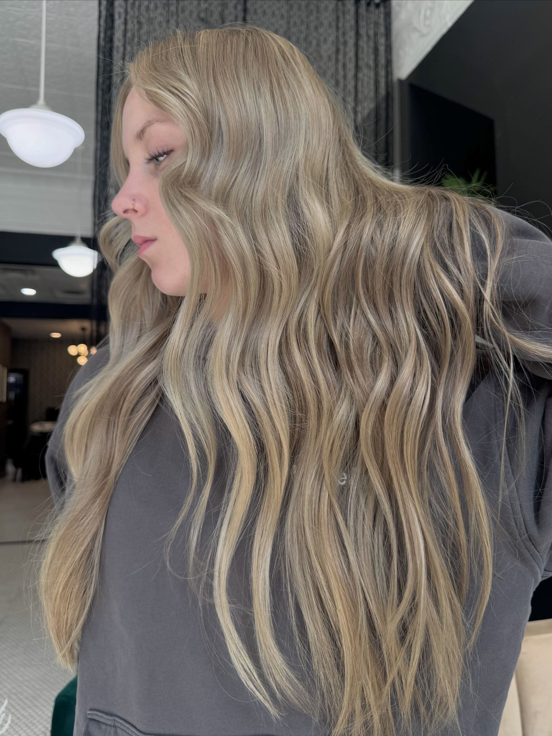 Side profile of a person with long wavy blonde hair wearing a dark gray top indoors