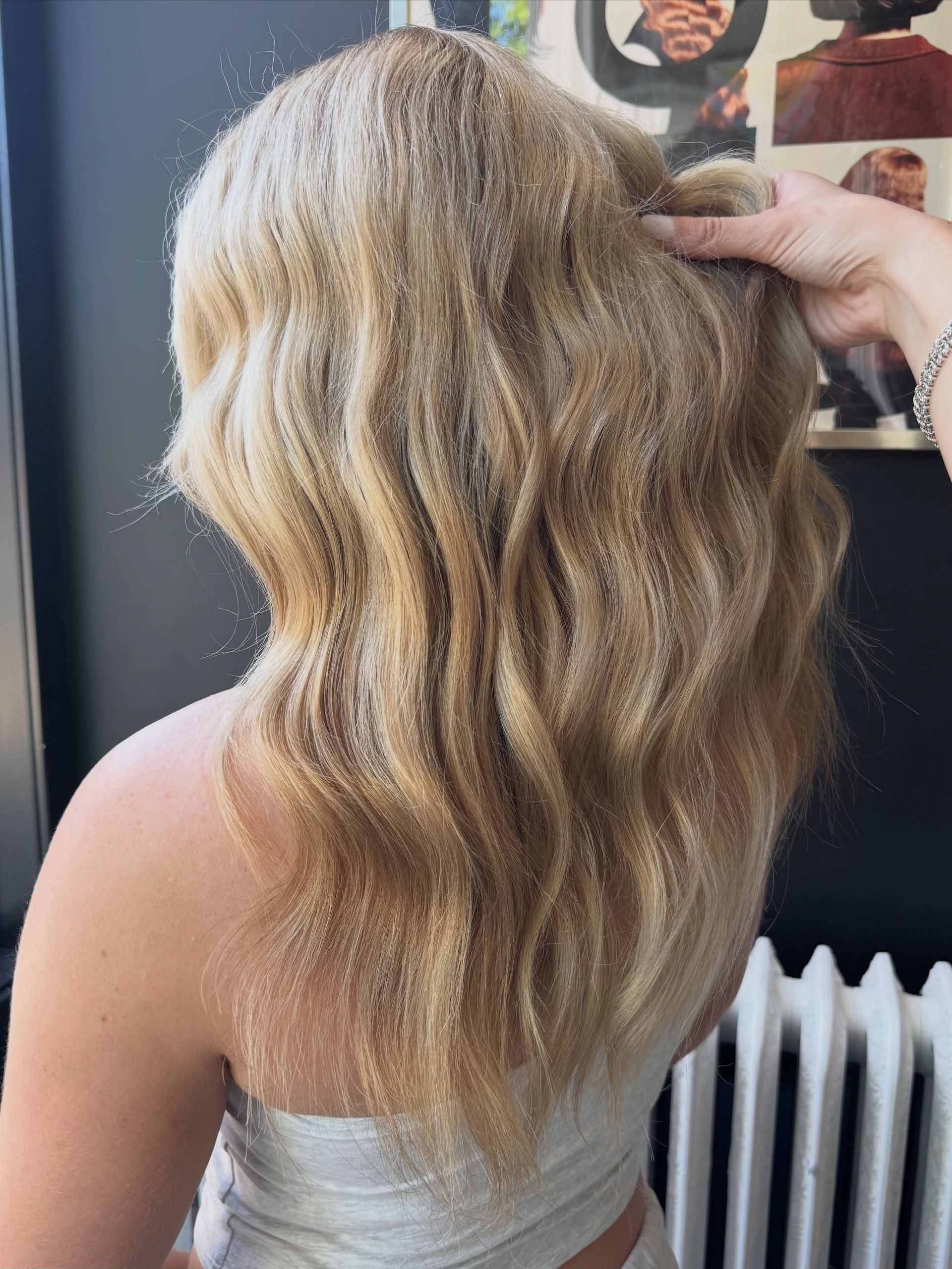 Wavy blonde hair styled in loose waves, shown from the back in a salon setting.