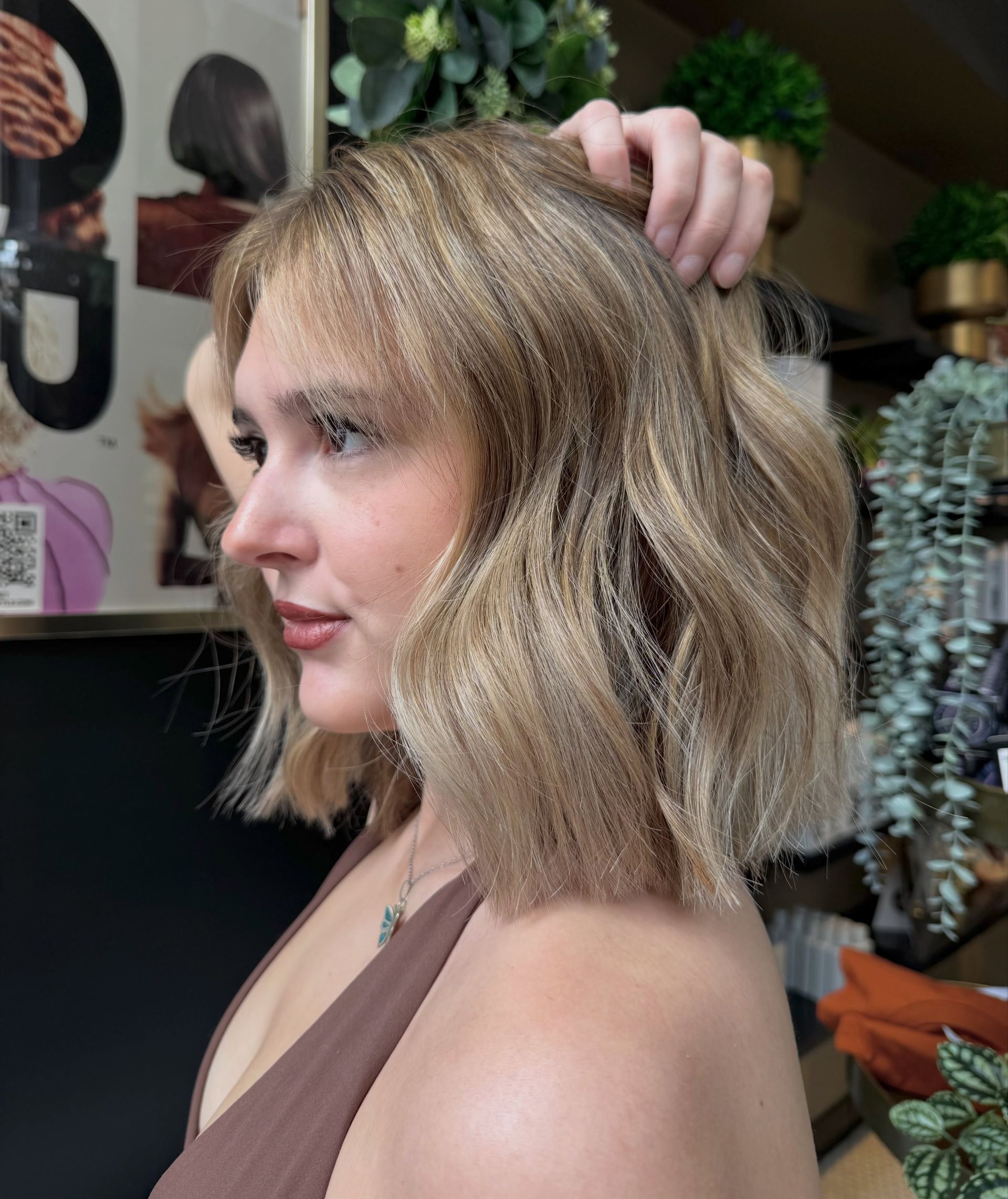 Woman with short blonde hair in a salon, touching her hair and posing in profile.