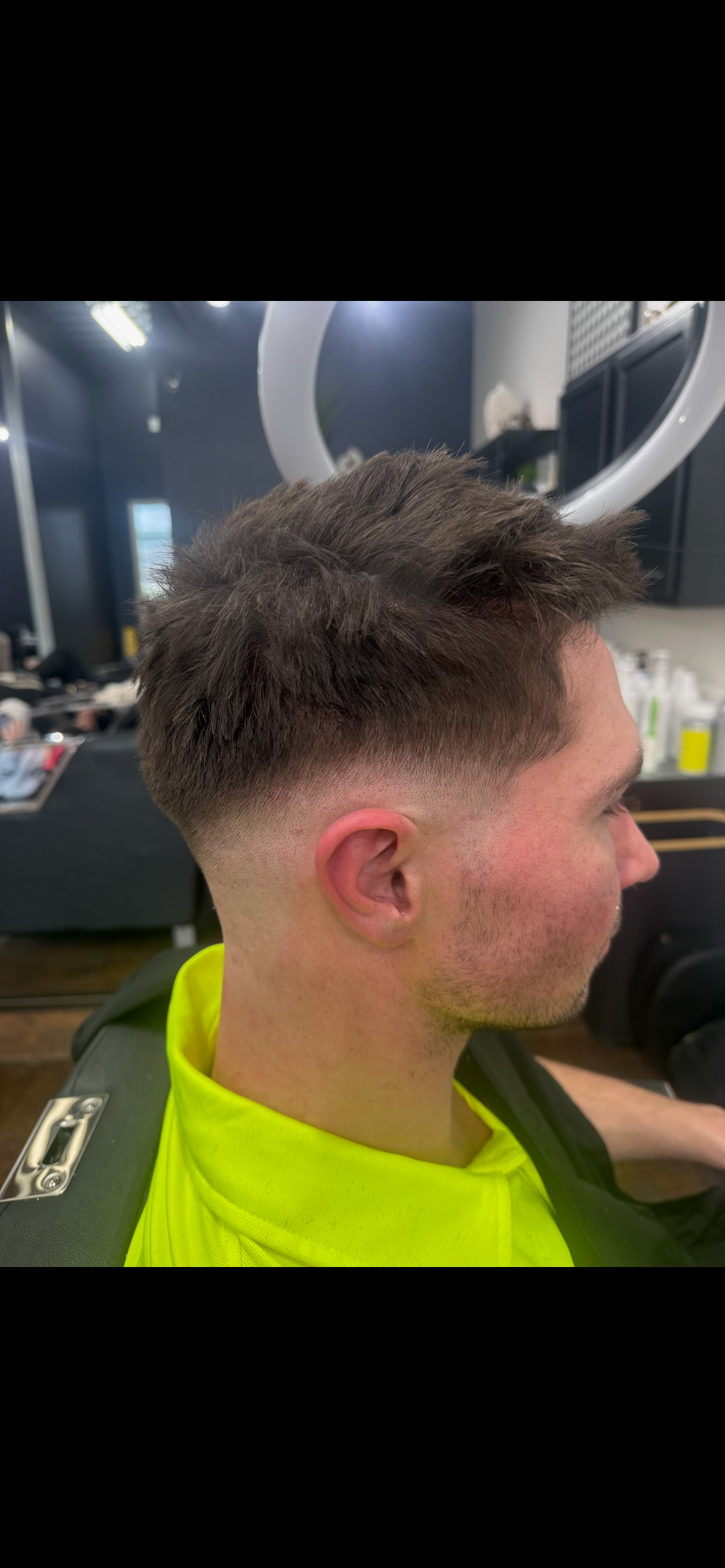 Side profile of a person with a fresh fade haircut and red ear in a barbershop chair