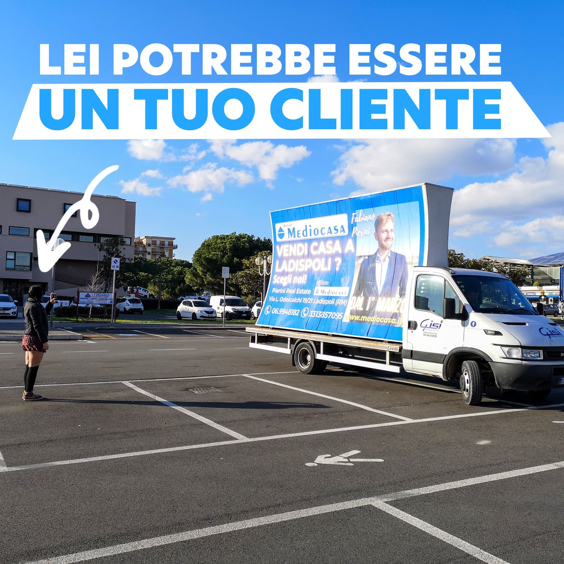 Una persona in un parcheggio indica un camion con un annuncio immobiliare recante la scritta 