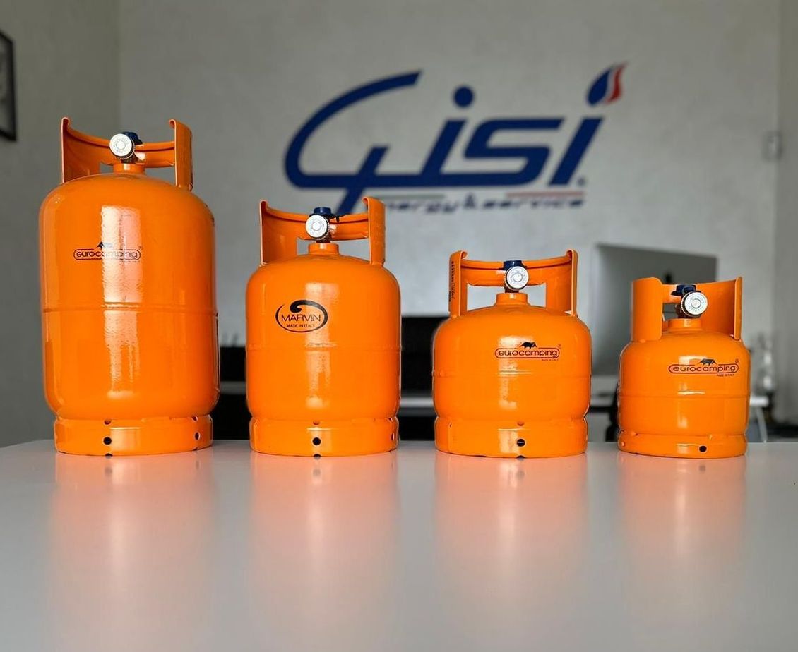 Quattro bombole di gas arancioni di diverse altezze disposte su un tavolo bianco davanti al logo dell'azienda Gisi.