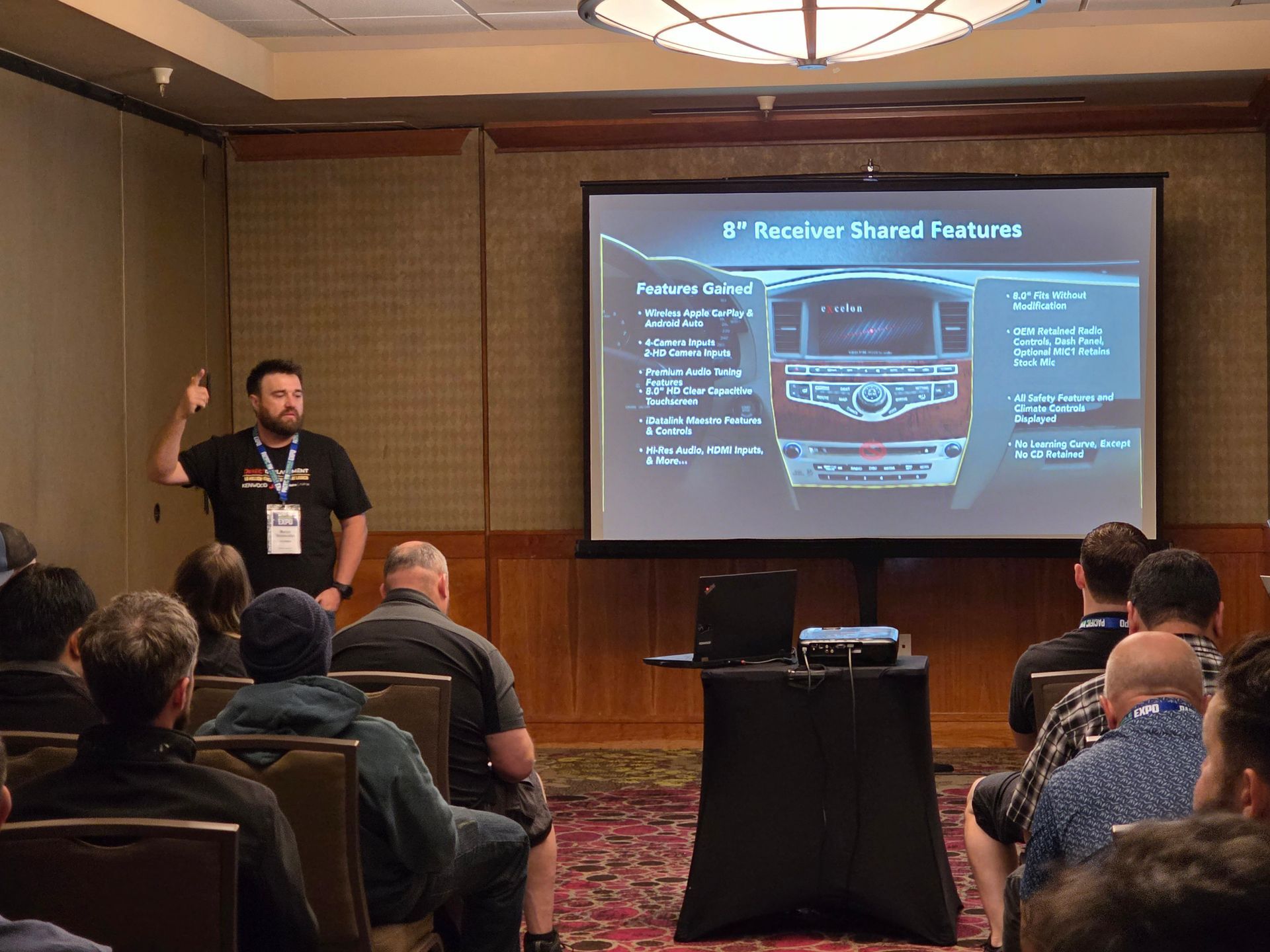 A speaker presents features of an 8-inch car receiver on a screen to an audience in a conference room.