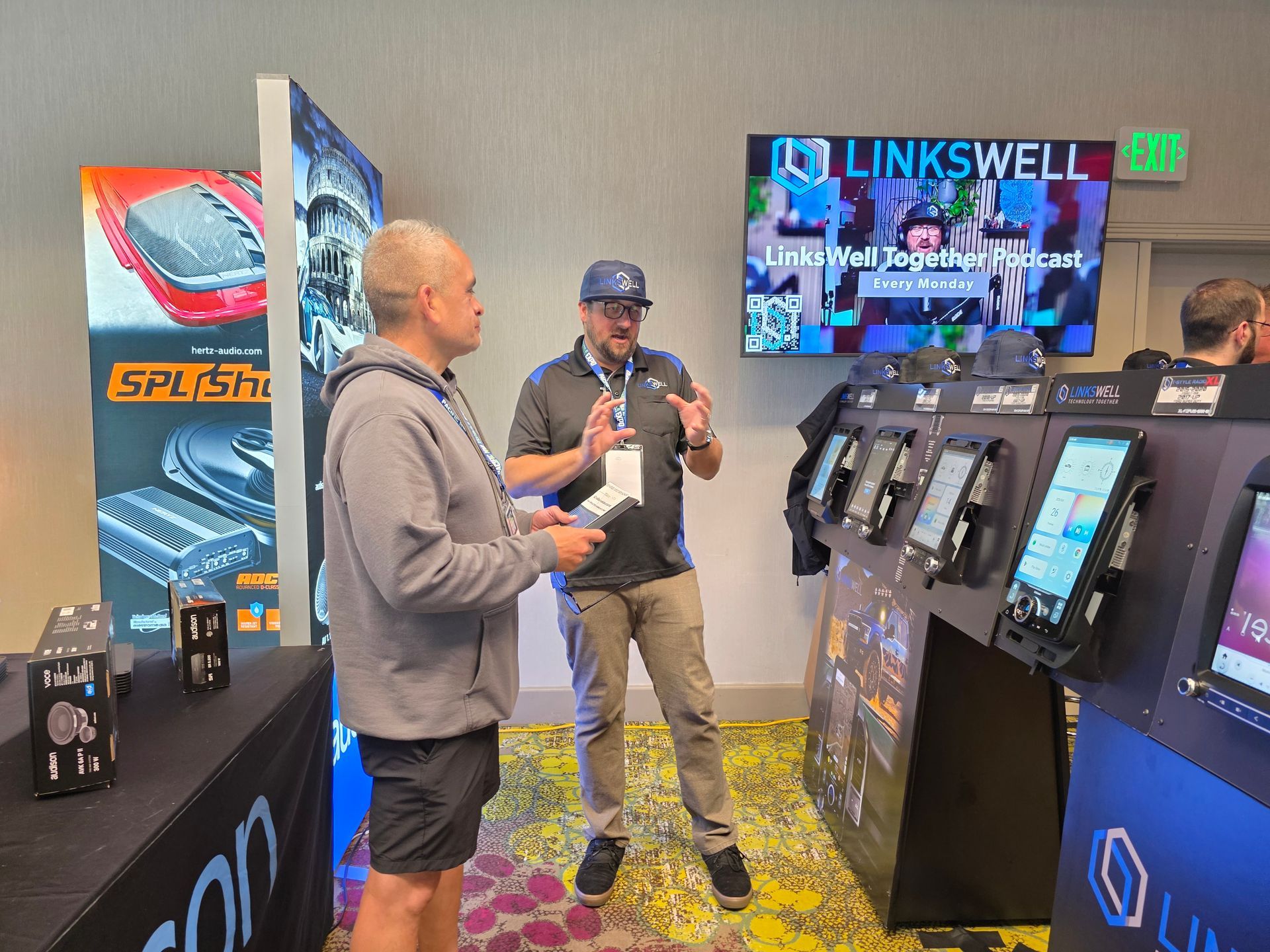 Two people talk at a Linkswell display booth featuring electronic screens and banners in a conference room setting.