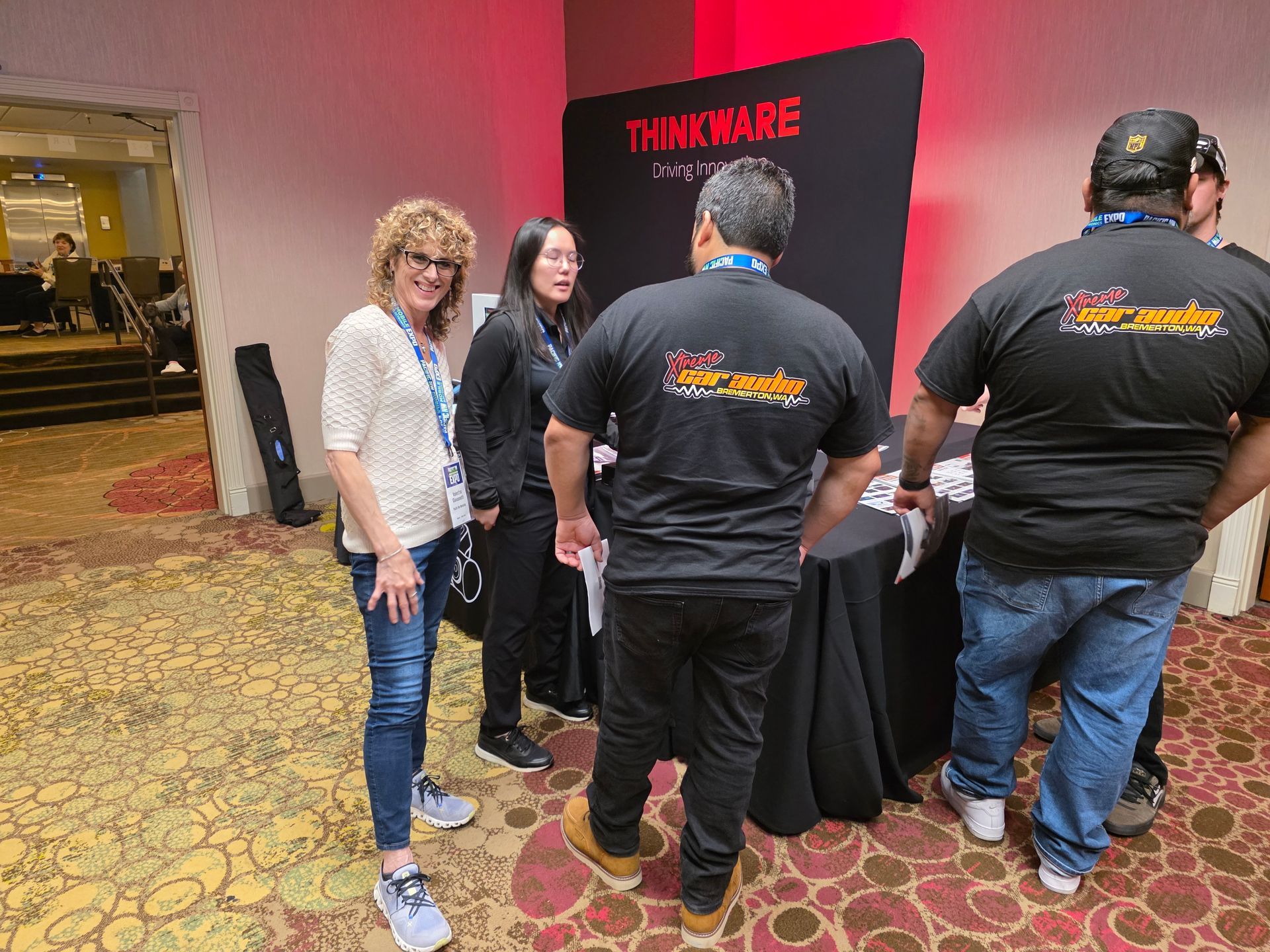 People gather at a Thinkware booth in a hotel ballroom, with two individuals in branded black shirts standing at a table.