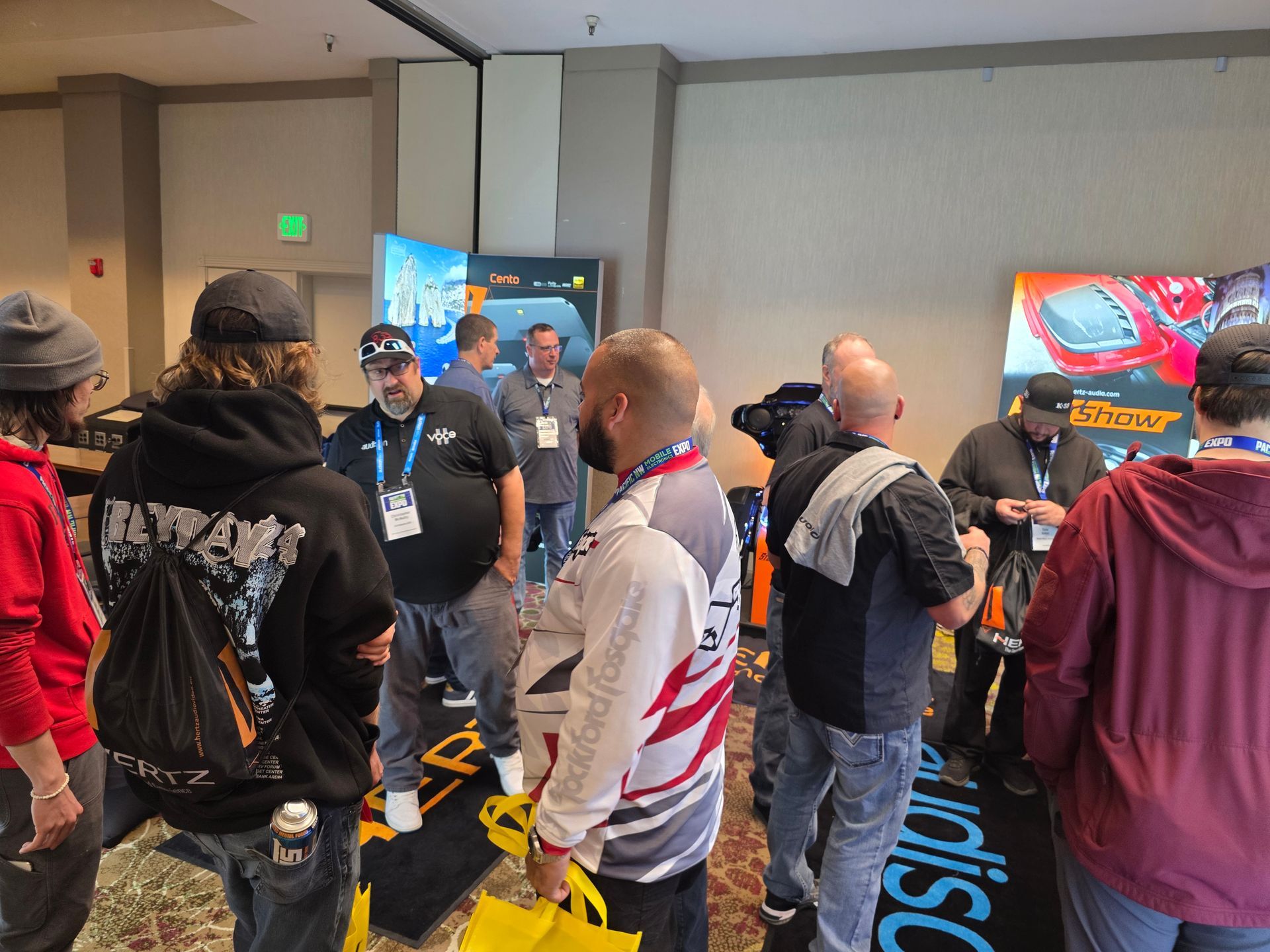 People gather at a conference trade show, interacting with displays and chatting in a convention center hallway.