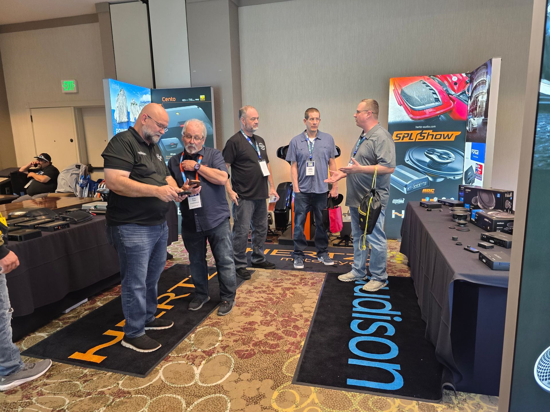 Five people gather at an indoor trade show booth displaying automotive products, engaged in conversation and looking down.