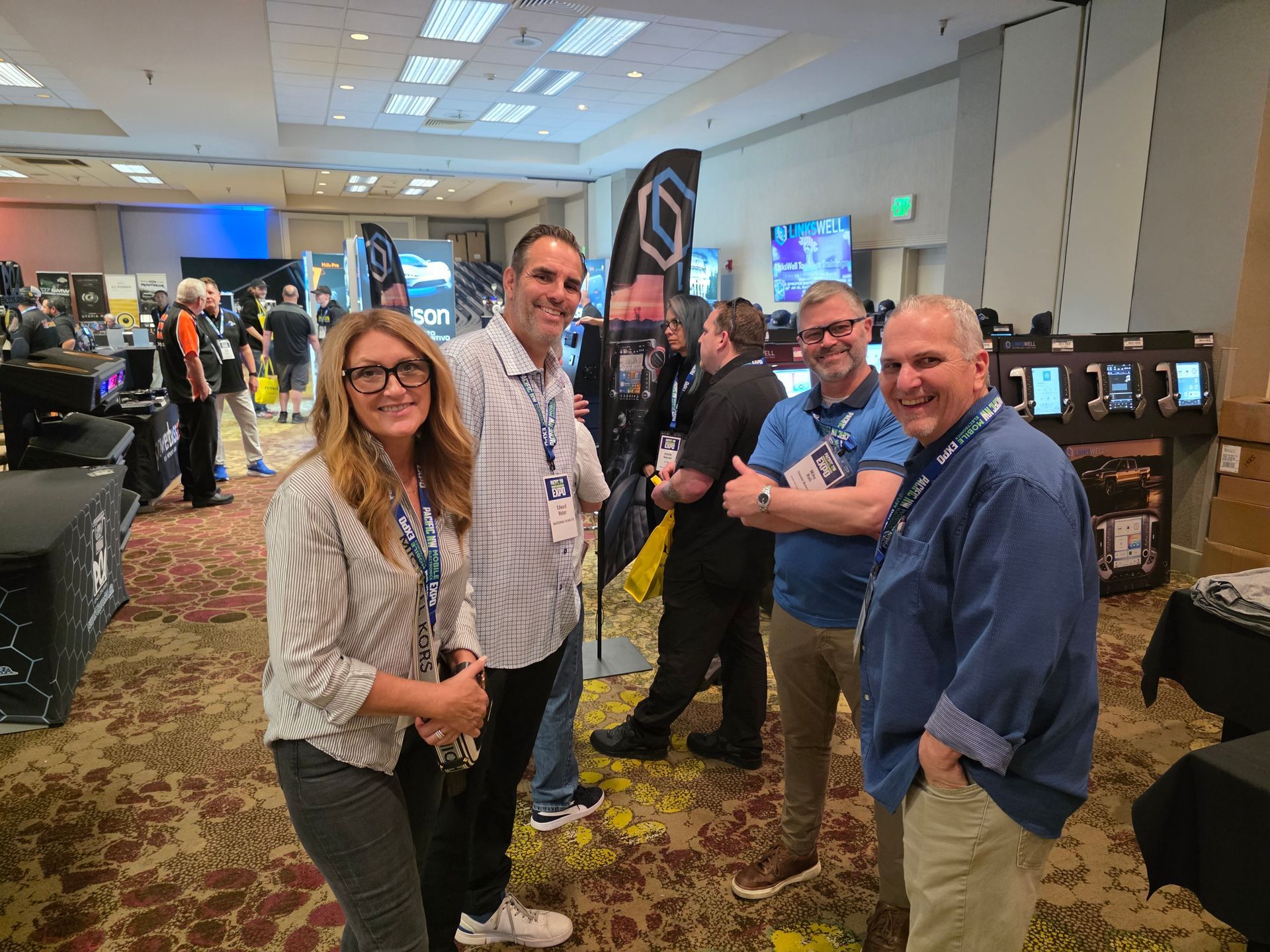 Four people stand smiling in a hotel ballroom during a professional convention, near trade show booths and displays.