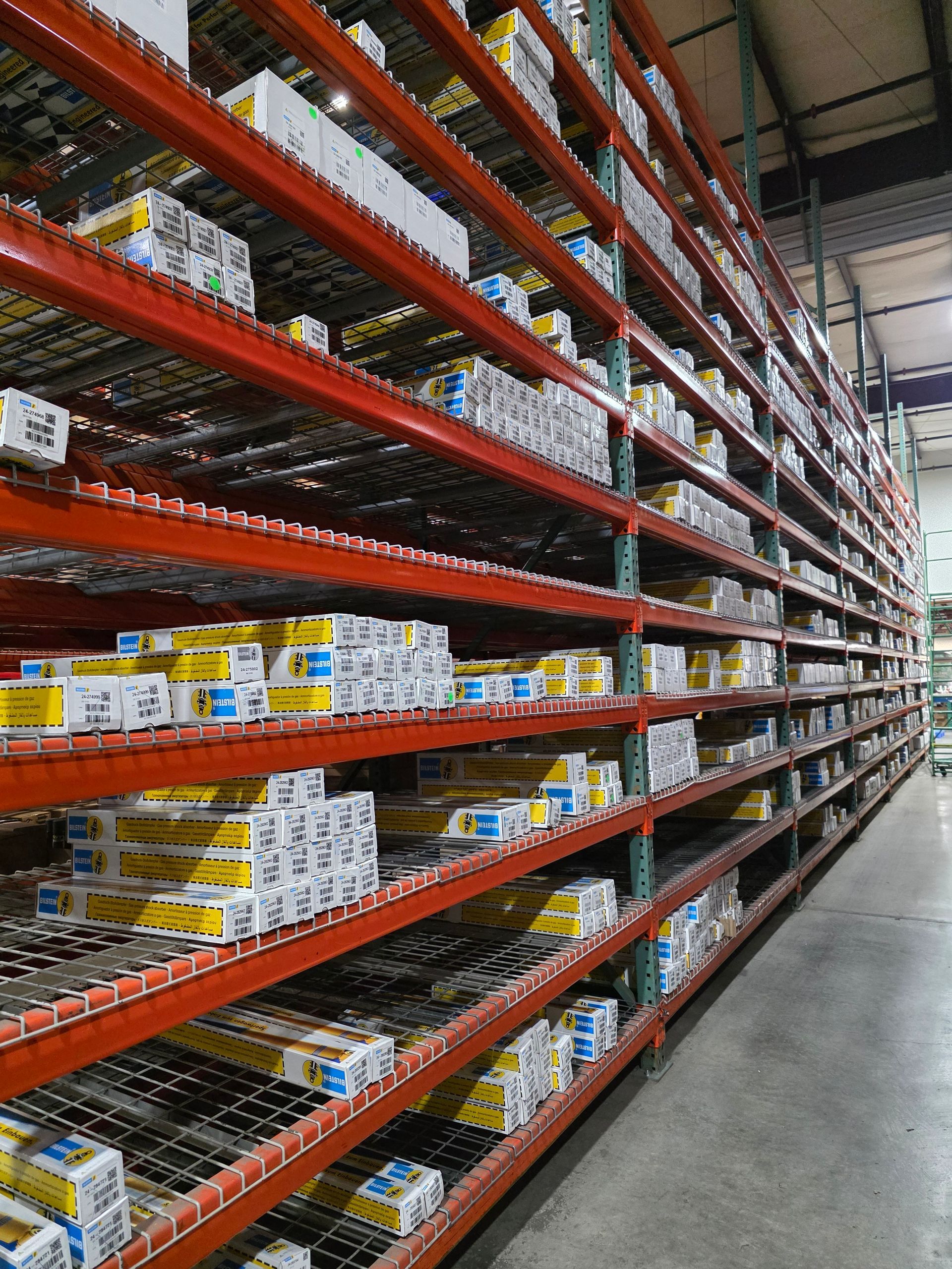 Tall orange industrial warehouse shelving units filled with rows of stacked boxes, extending into the distance.