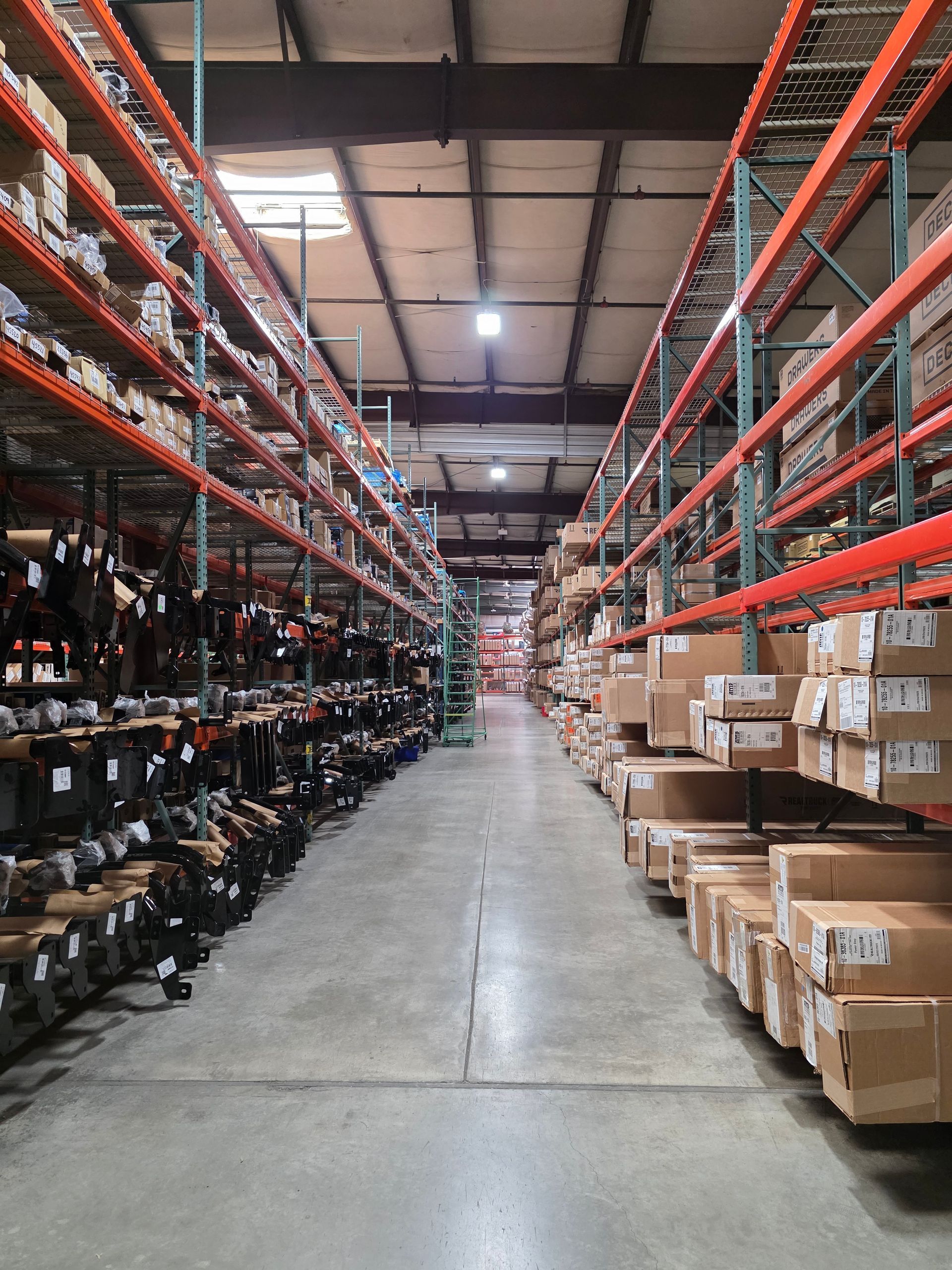A long aisle in a warehouse with industrial orange shelving stacked with inventory on both sides.