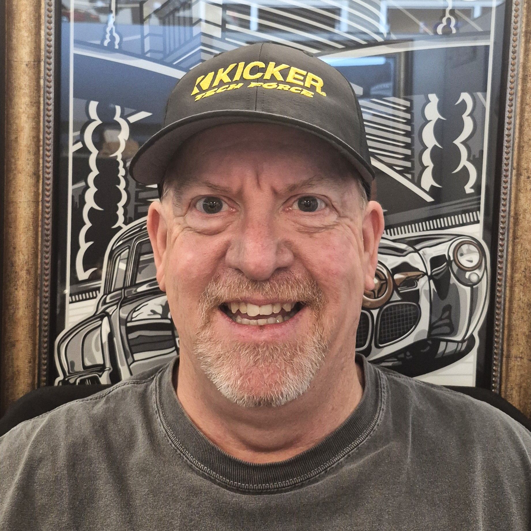 A smiling person wears an orange and black baseball cap and a textured red collared shirt, shown against a neutral wall.