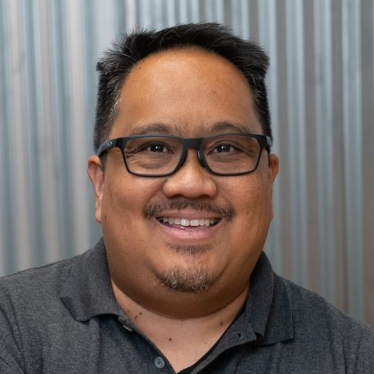 Man smiling in a dark shirt against a gray and black patterned backdrop