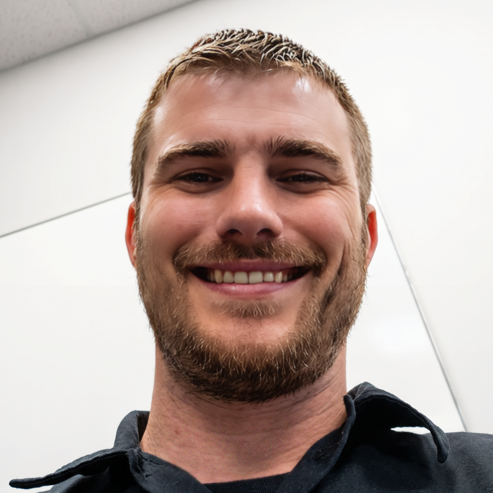 Man smiling in a dark shirt against a gray and black patterned backdrop