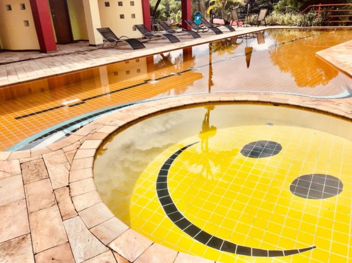 Piscina vazia com um mosaico amarelo de carinha sorridente na parte rasa e água ao fundo.