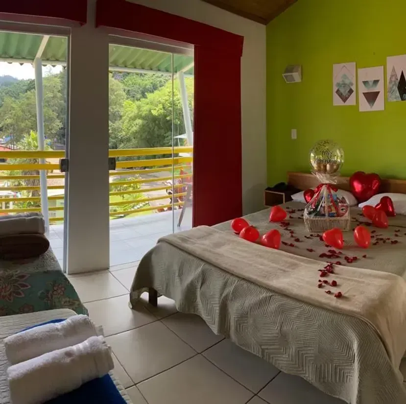 Quarto com cama de dossel, almofadas verde-claras, decorações florais e arte na parede.