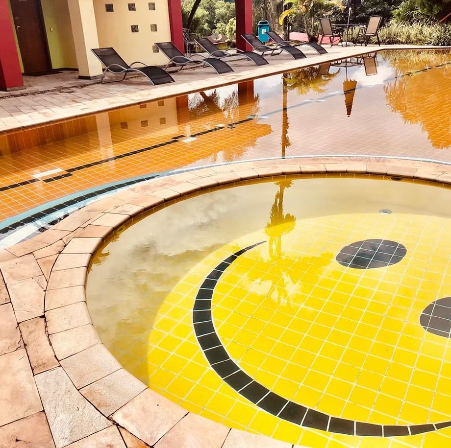 Duas mulheres em uma piscina, tomando champanhe em boias vermelhas sob um céu ensolarado em um resort.