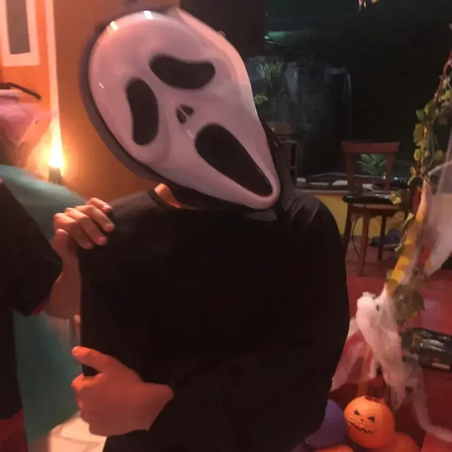 Pessoa com máscara do Ghostface segurando um telefone em um quarto decorado para o Halloween.