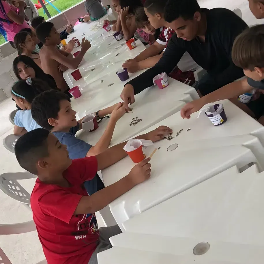 Crianças compartilhando bebidas em uma longa mesa branca durante uma festa ou evento.