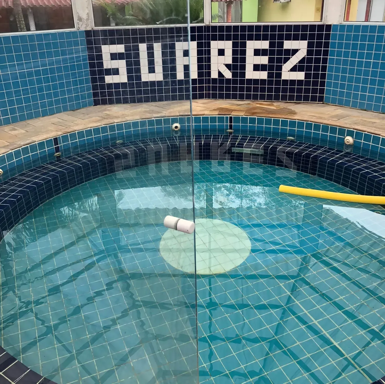 Piscina azul com azulejos, um brinquedo flutuante e uma placa na parede com a inscrição “SOAREZ”.