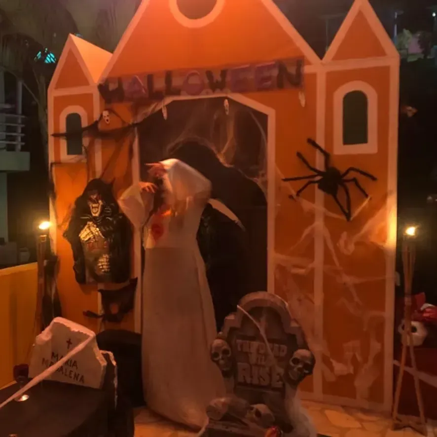Fachada de casa laranja decorada para o Halloween com fantasmas, uma aranha e uma lápide.