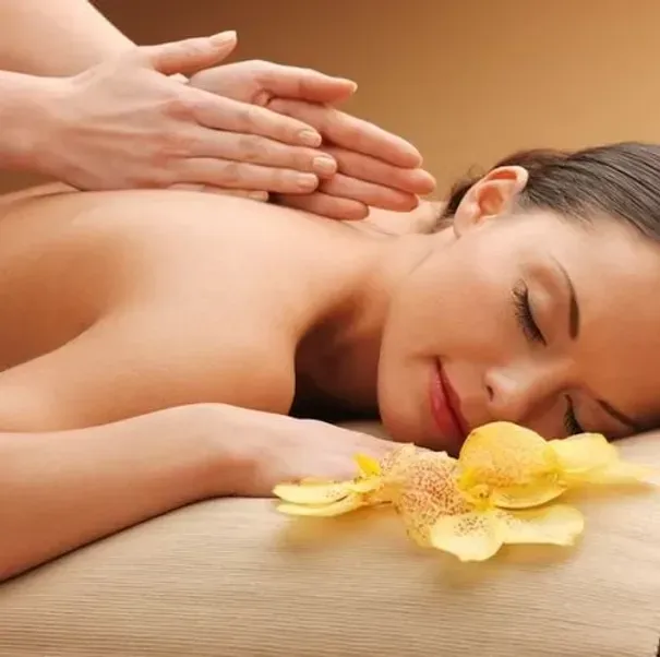 Massagem de spa com as mãos nas costas de uma mulher e o rosto adormecido ao lado de flores amarelas.