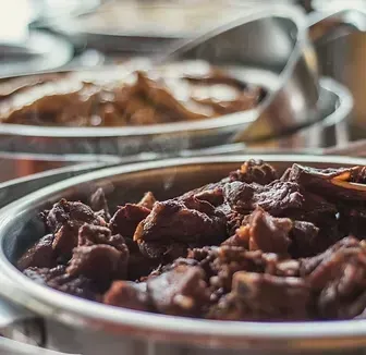 Close-up de tigelas de metal cheias de carne escura cozida lentamente em um bufê.