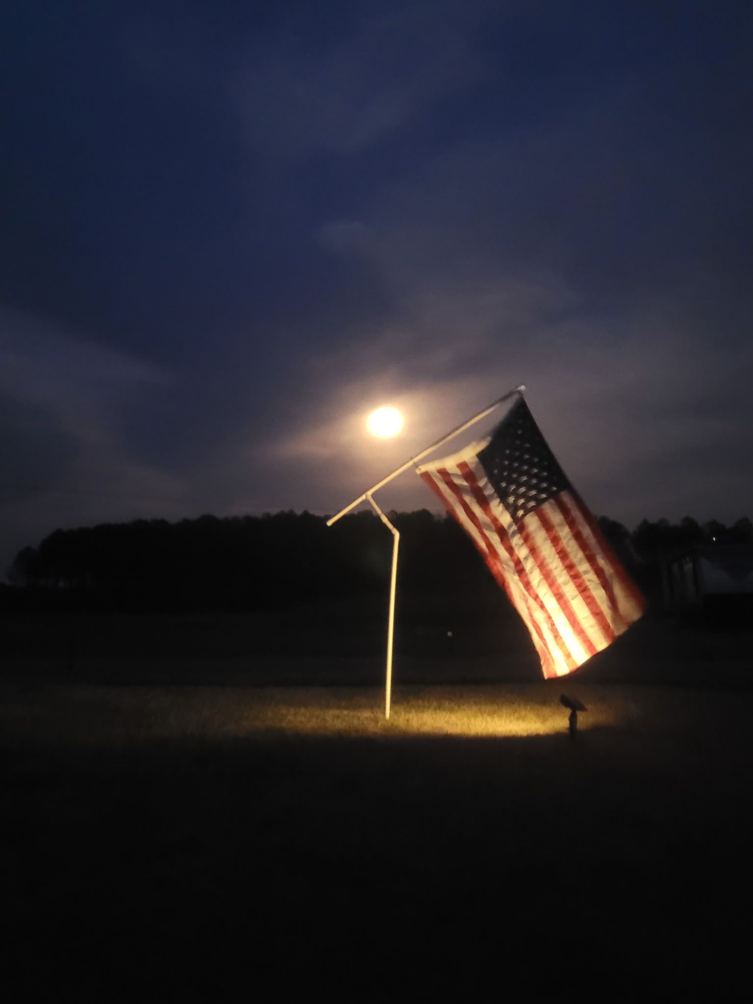 American flag lit at night, hanging from a white pole against a dark sky.