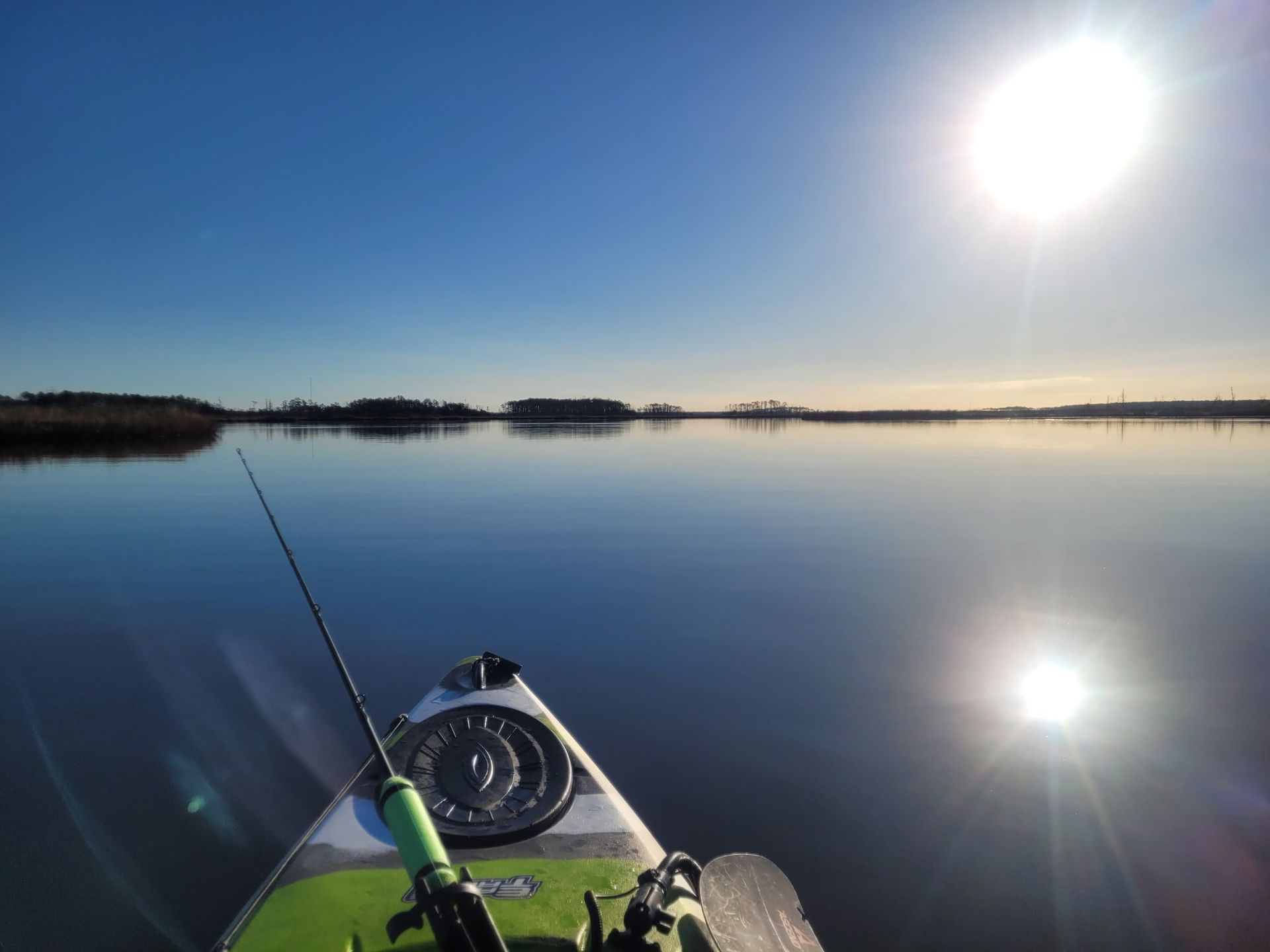 Kayak bow on a calm lake at sunrise, with bright sun and its reflection on the water.