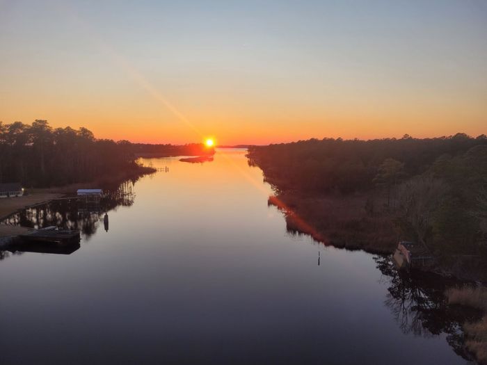 Sunset over a calm river with silhouetted trees and a small dock on the left