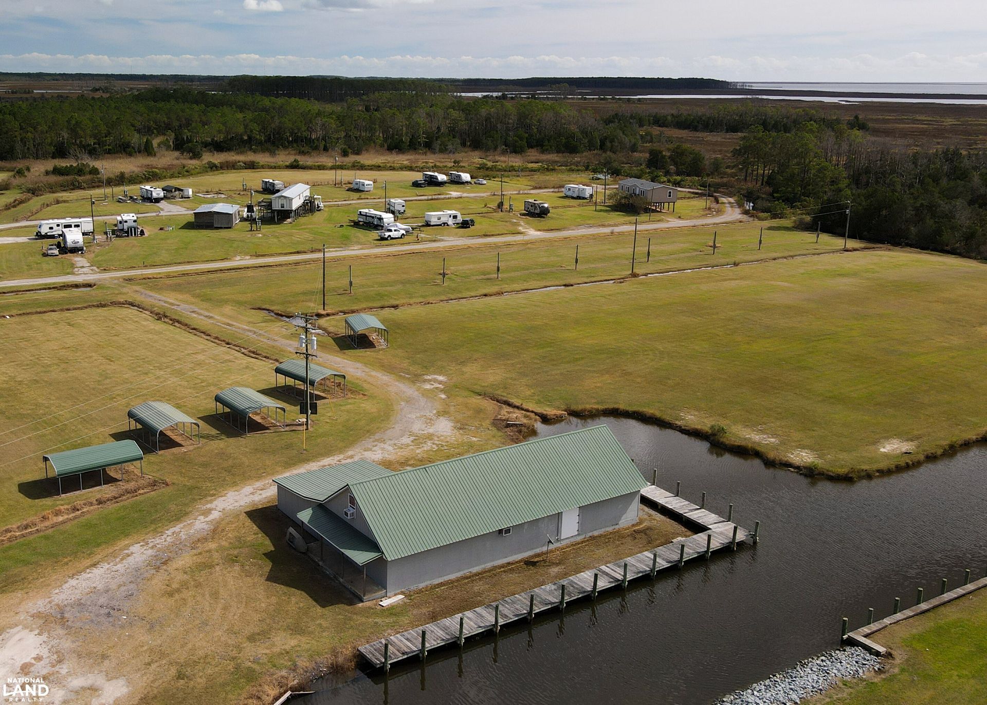Aerial view of a rural campground with RVs, grassy fields, and a lakeside boathouse with a dock