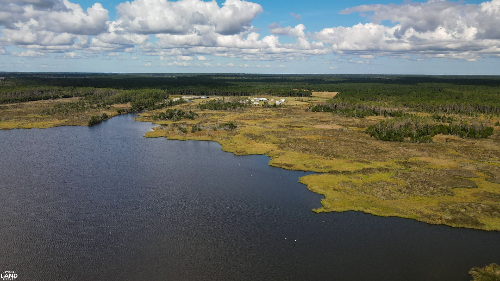Aerial view of a dark lake beside green marshland under a cloudy sky