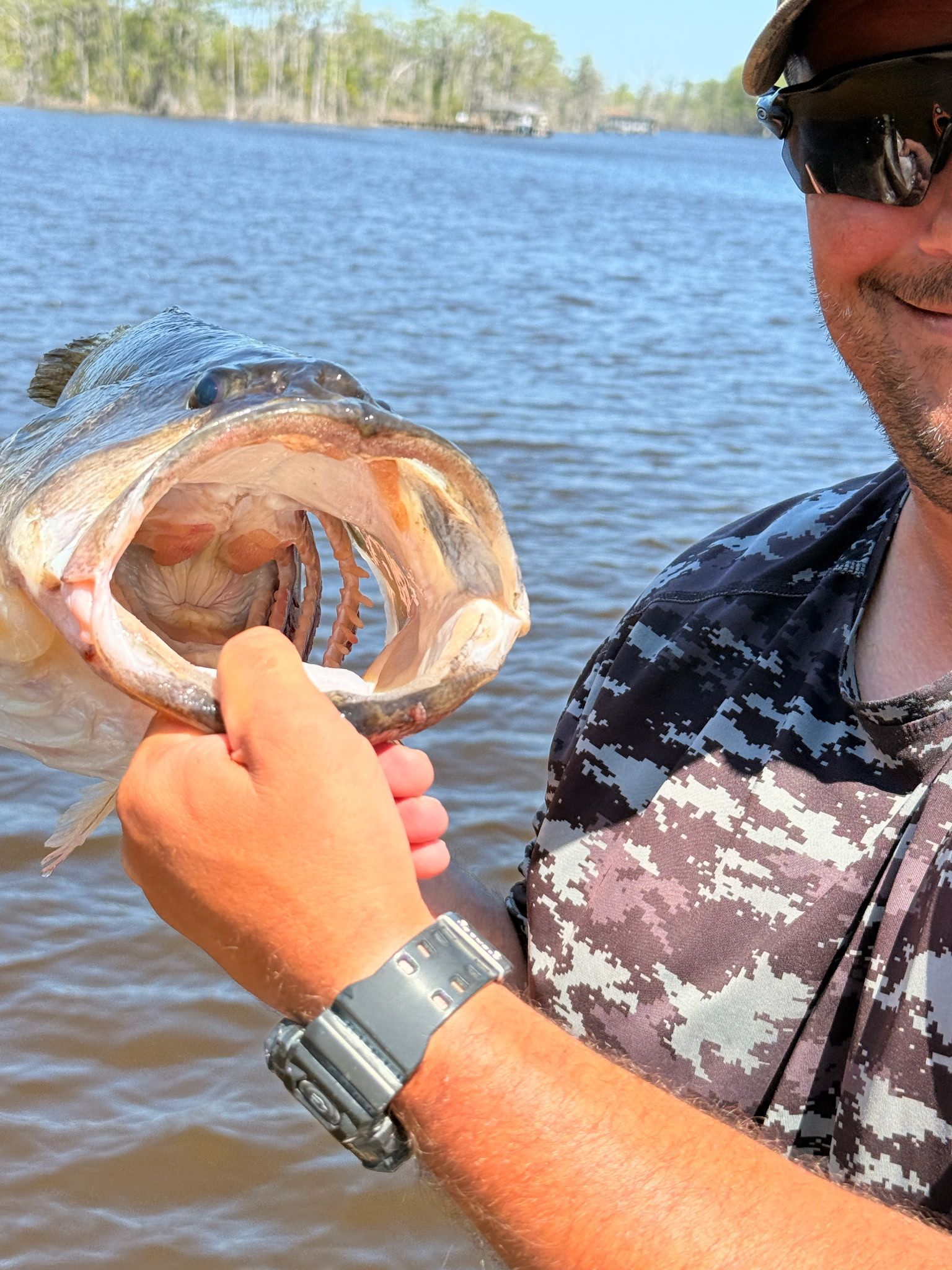 Angler holding a fish open by the mouth on a boat, with lake and trees in the background