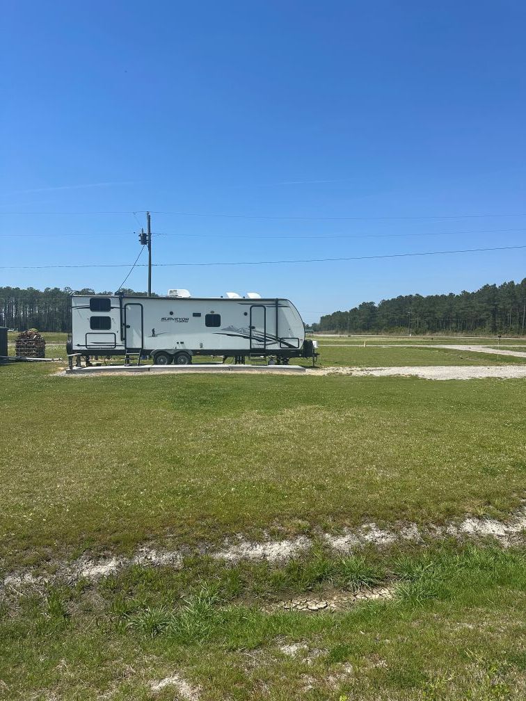 White RV parked on a grassy field under a clear blue sky with trees in the distance