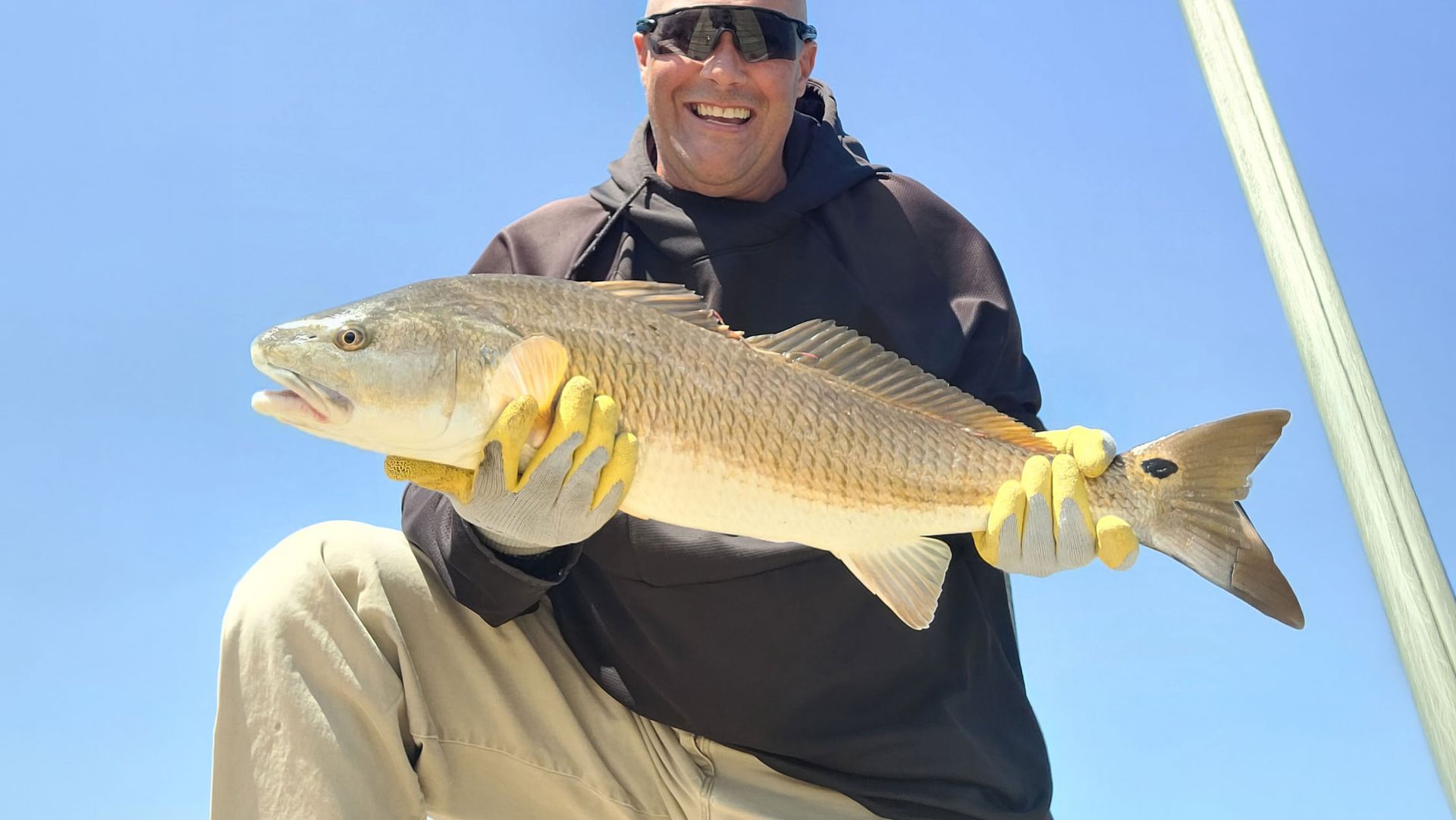 Smiling angler holding a large fish against a clear blue sky